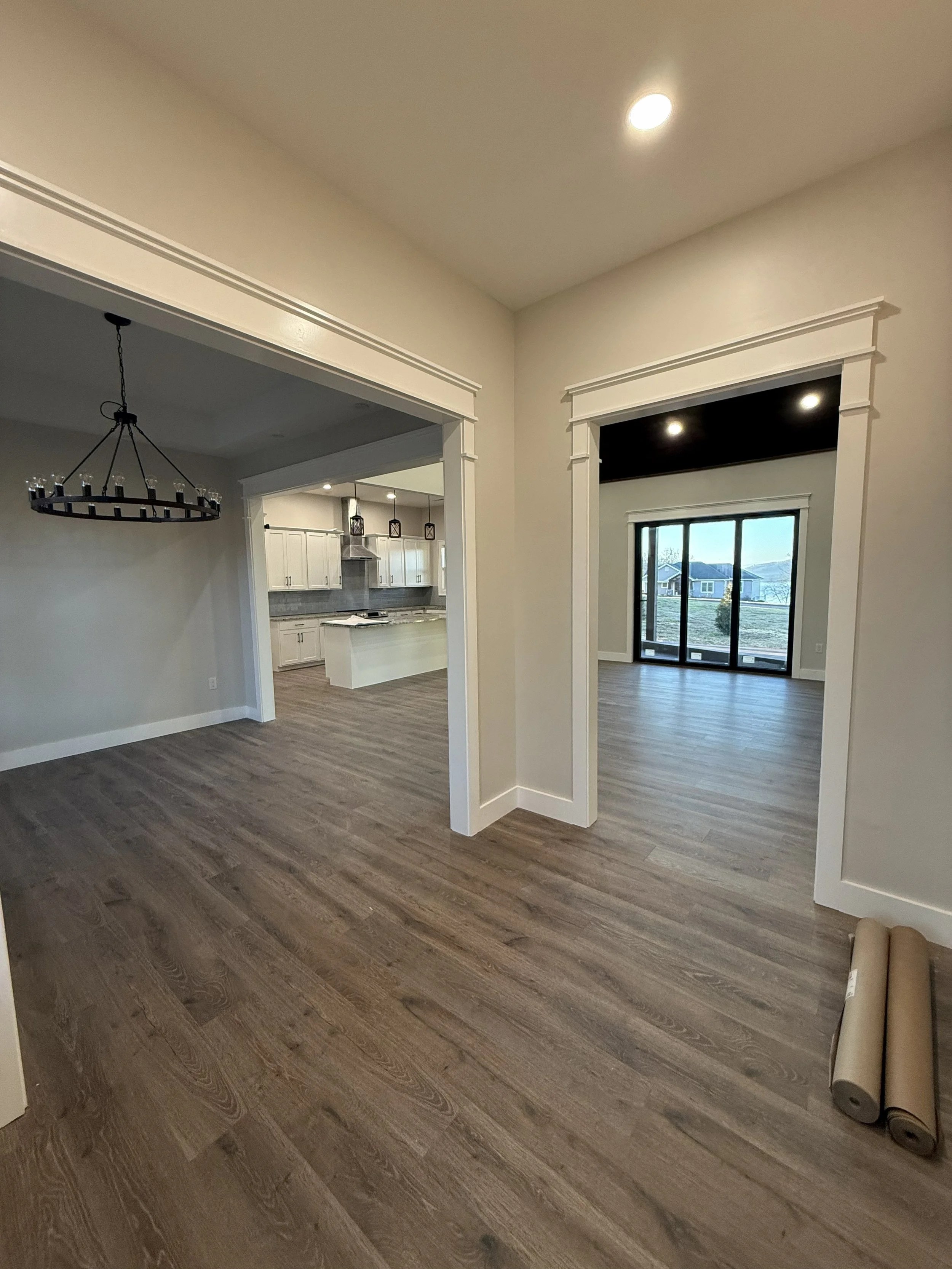 Empty living area with brown wood flooring, open kitchen with white cabinets, and a sliding glass door leading outside.