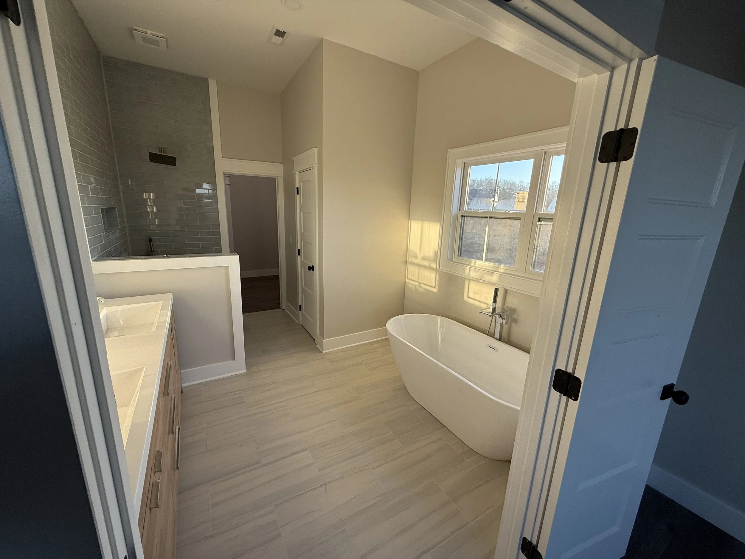 Modern bathroom with a freestanding bathtub, a window with sunlight, a double vanity sink, and a walk-in shower with gray subway tiles.