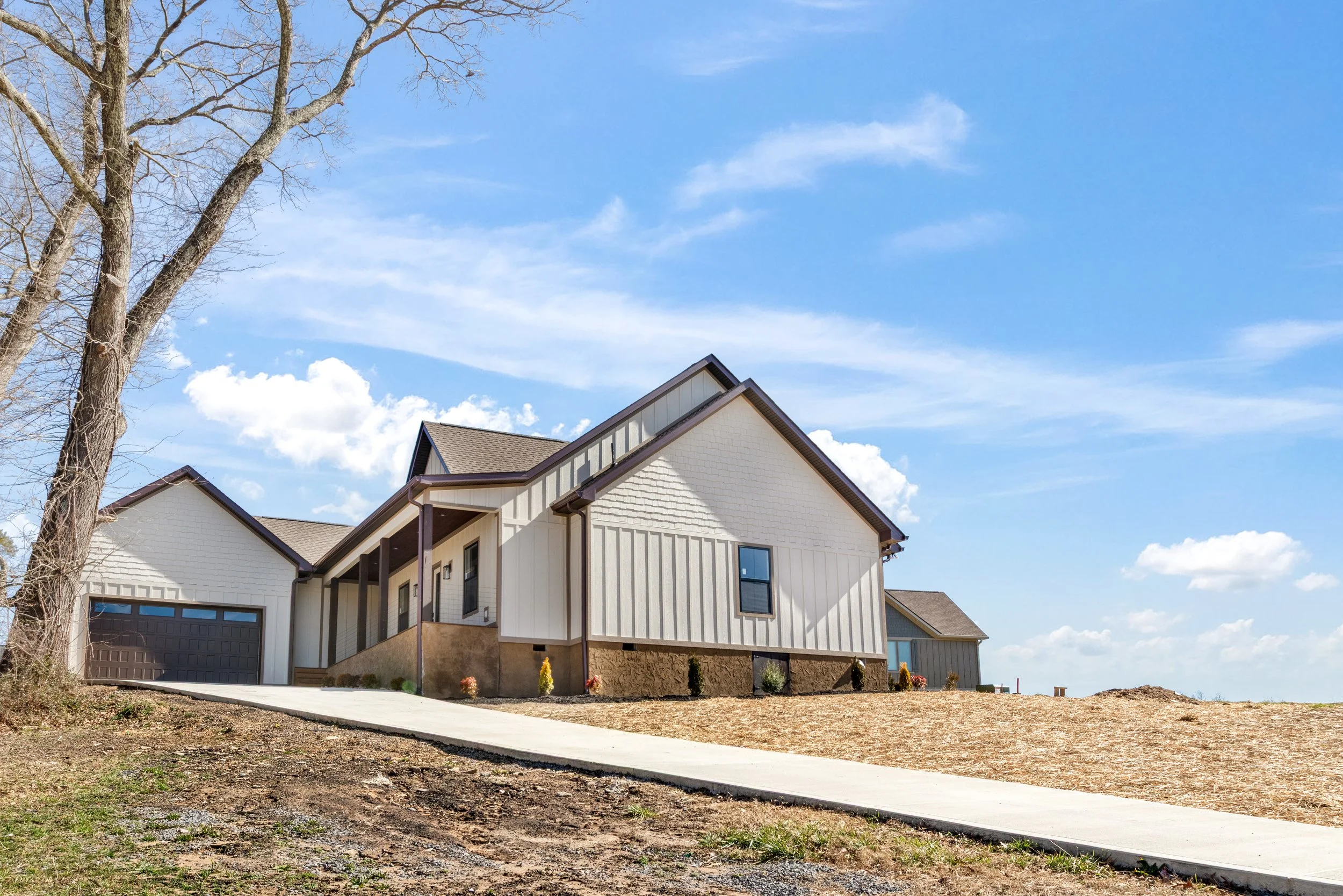 Modern house with white siding and black trim, situated on a sloped lot, under a blue sky with clouds.