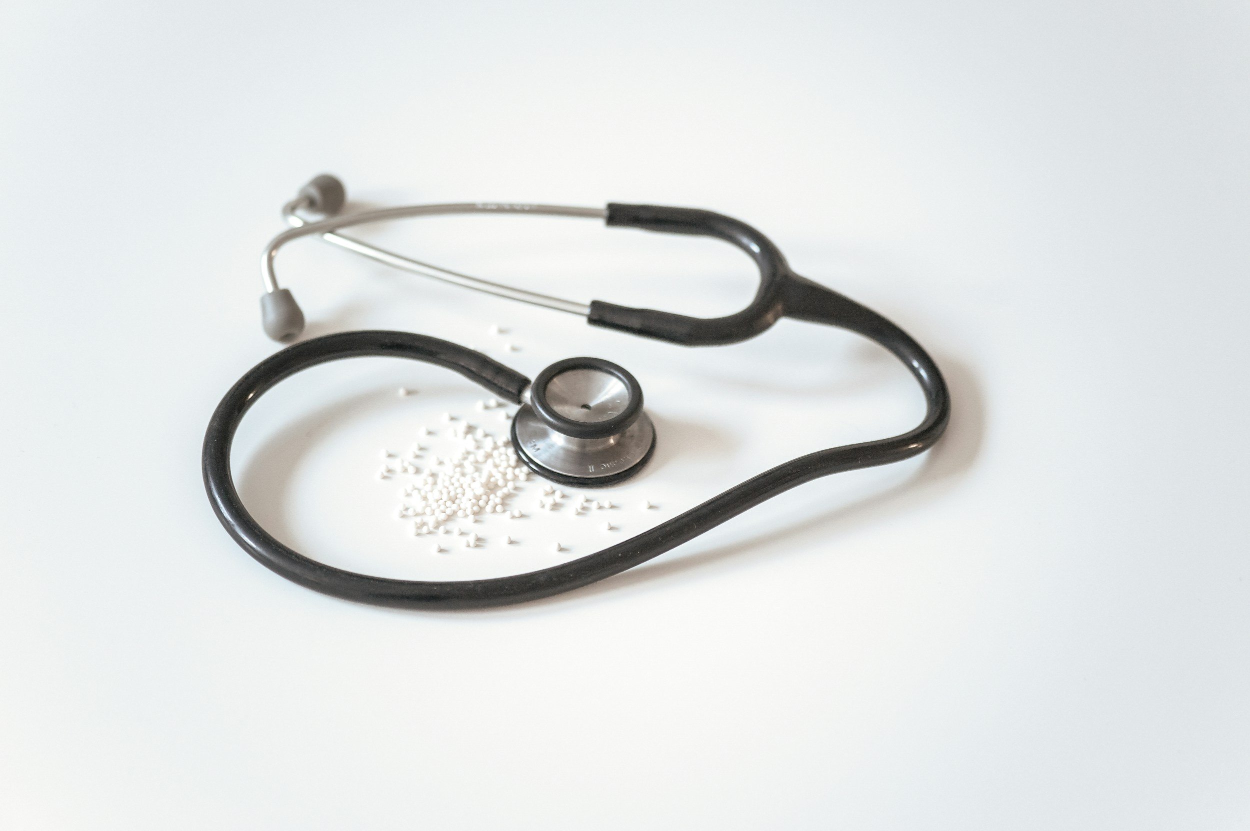 A stethoscope and small white pills on a white surface.