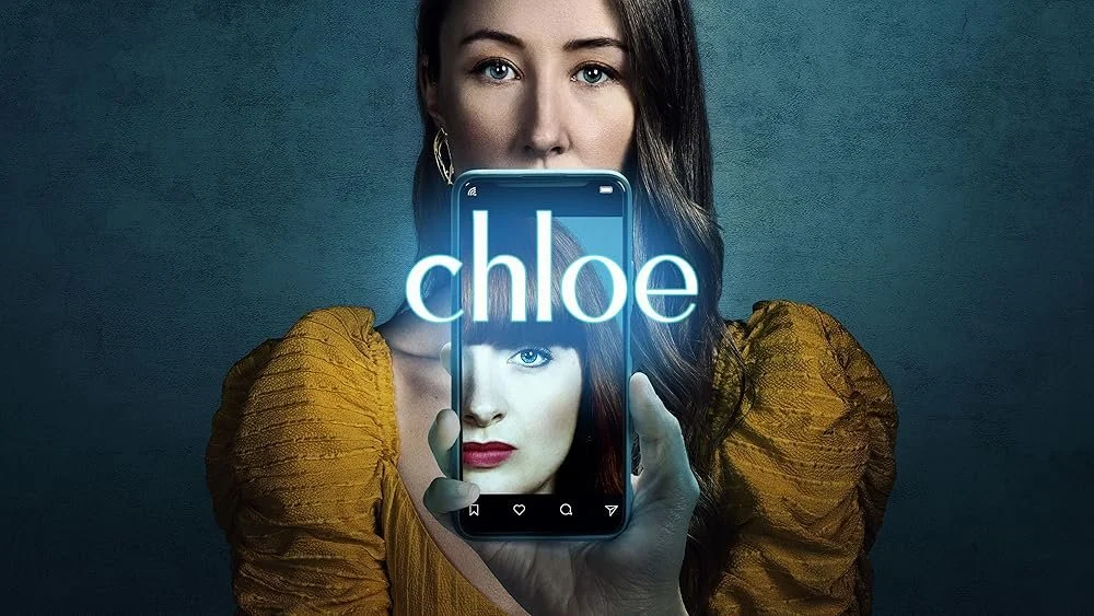 A woman with wavy hair, wearing a mustard yellow top with puffed sleeves, holds a smartphone with a mirror image of her face on the screen. The phone displays the word 'Chloe' in large text overlaying her reflection.