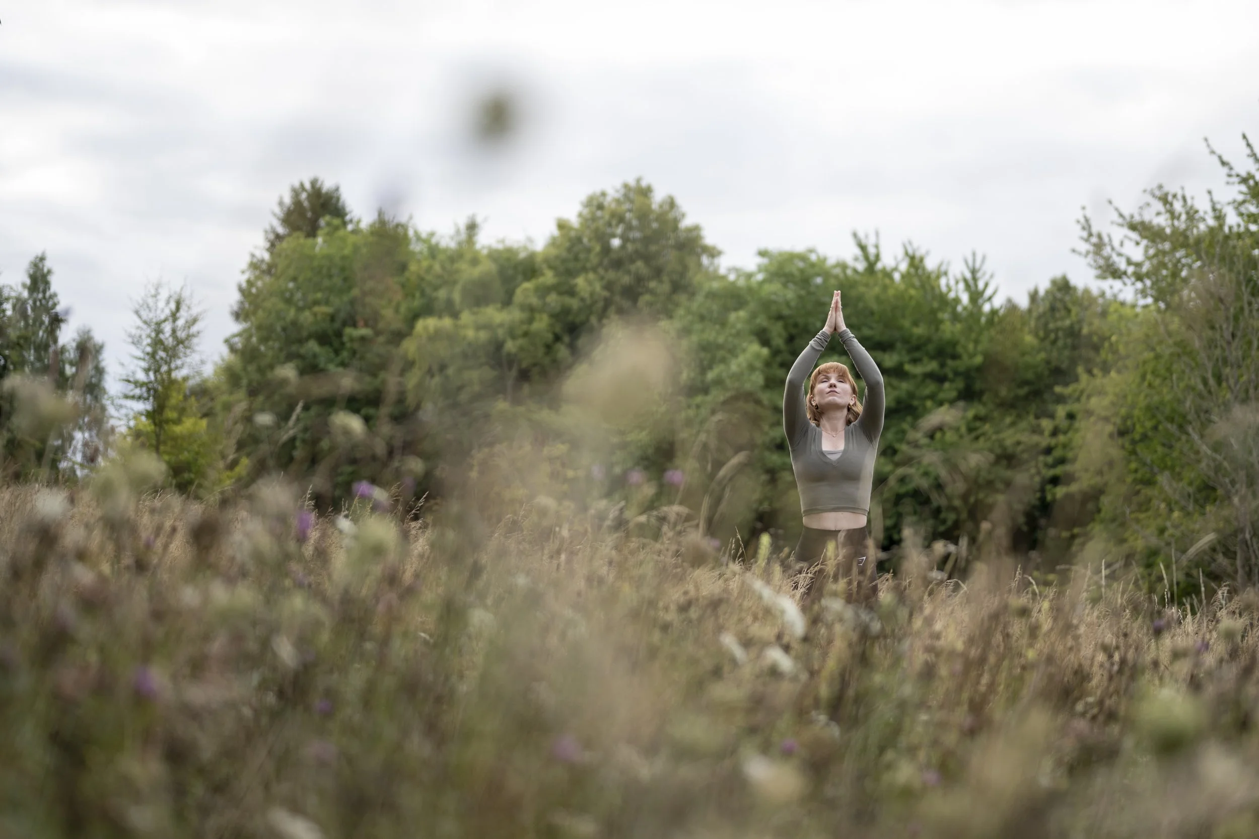 Yoga teacher in Saffron Walden Vicky Cook from Pause Breath Flow. Standing in a field near Saffron Walden performing a yoga pose with hands in prayer to the sky ready to start a yoga flow sun salutation Surya Namaskar A.