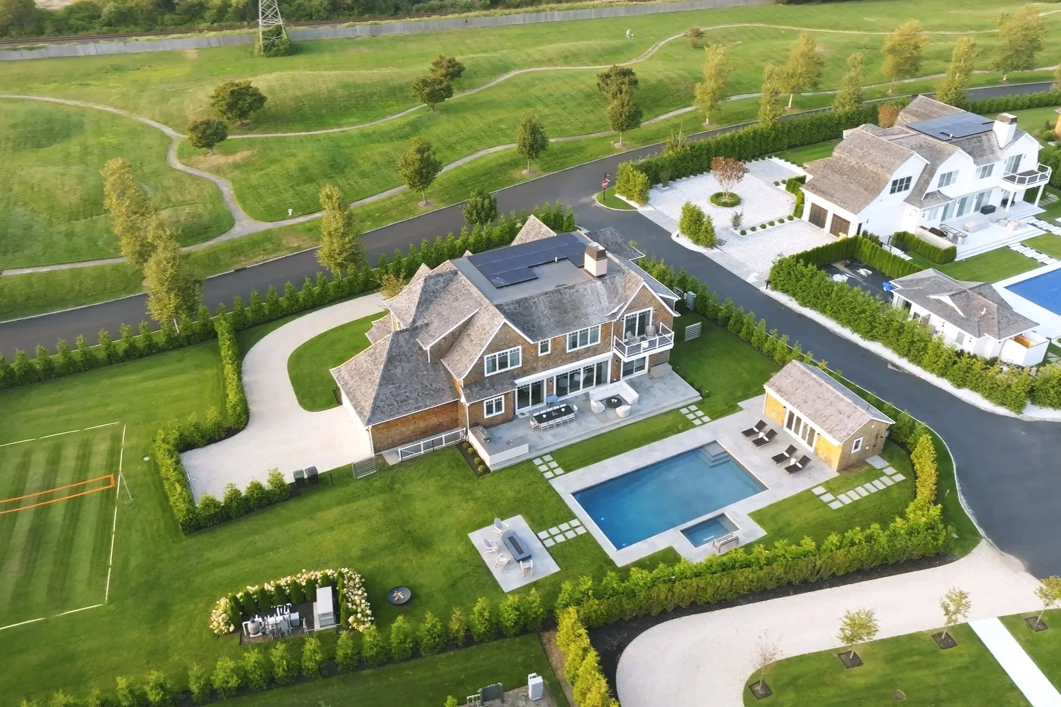 Aerial view of a residential neighborhood with large houses, swimming pools, manicured lawns, and landscaping.