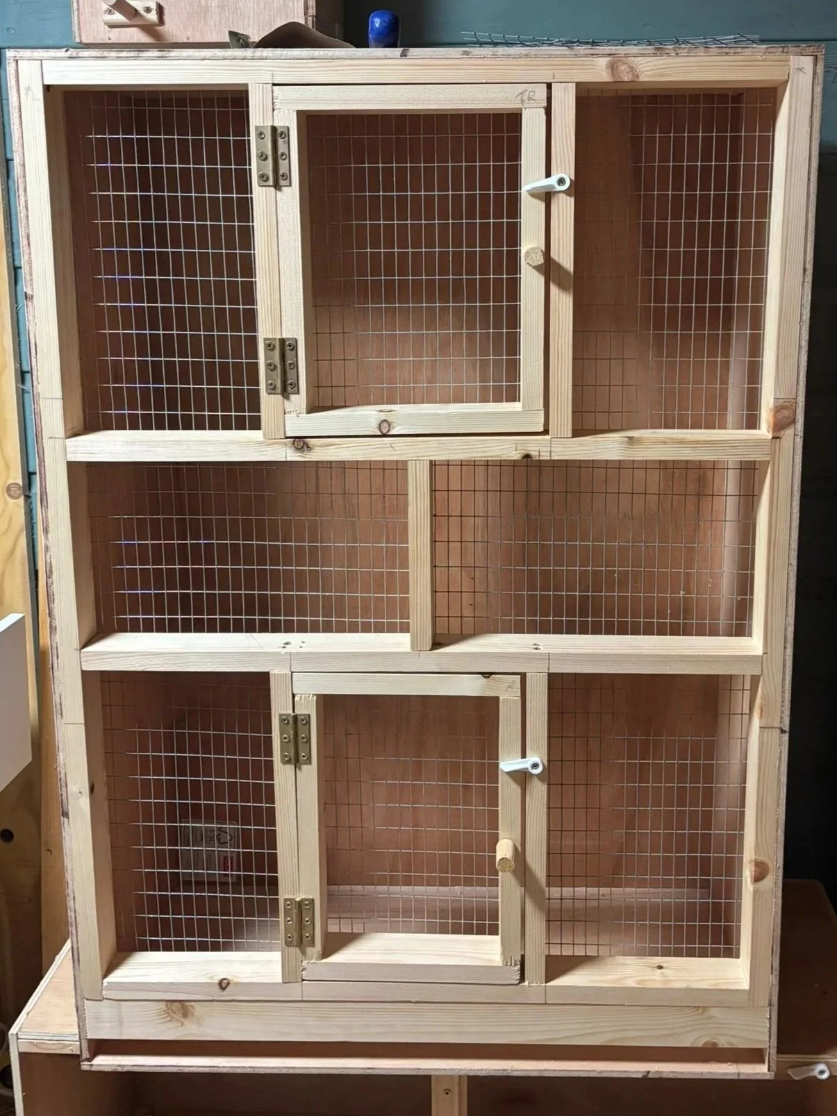 A wooden animal enclosure with multiple compartments, featuring wire mesh doors and small latches, likely used for small animals or pets.