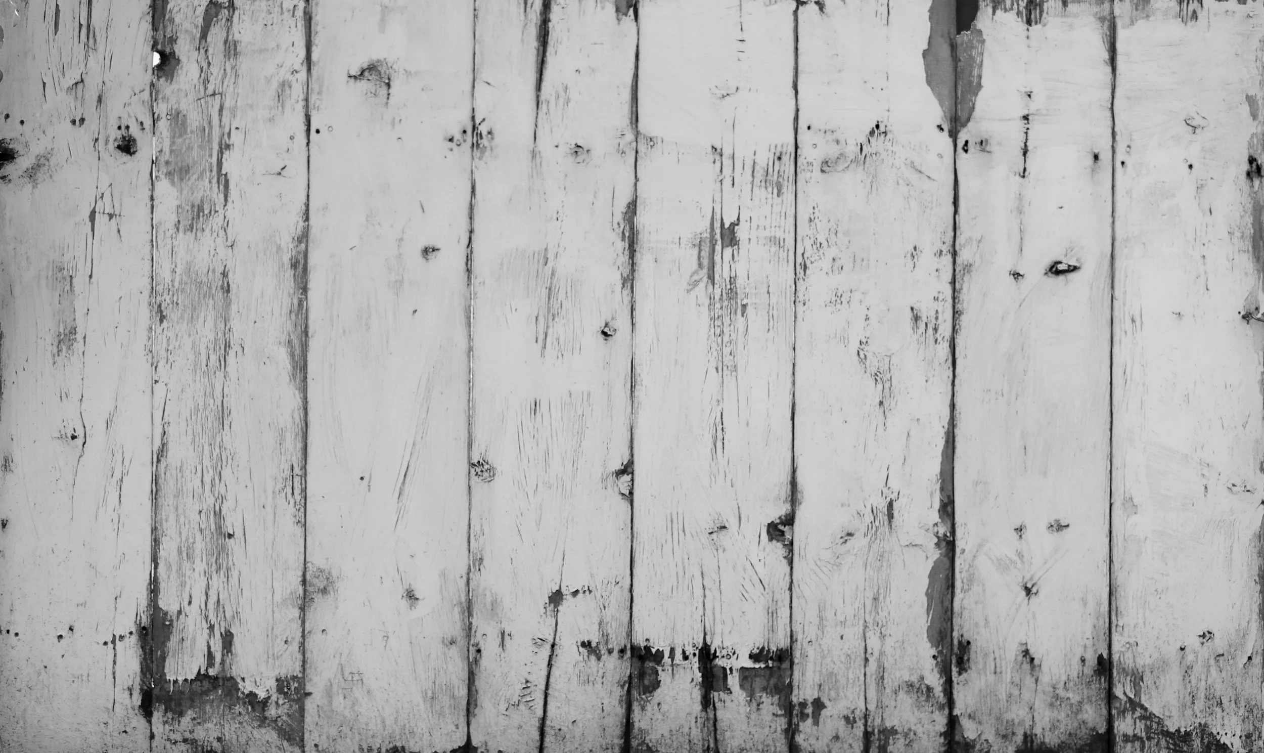 Black and white photograph of weathered wooden planks with peeling paint and visible knots.