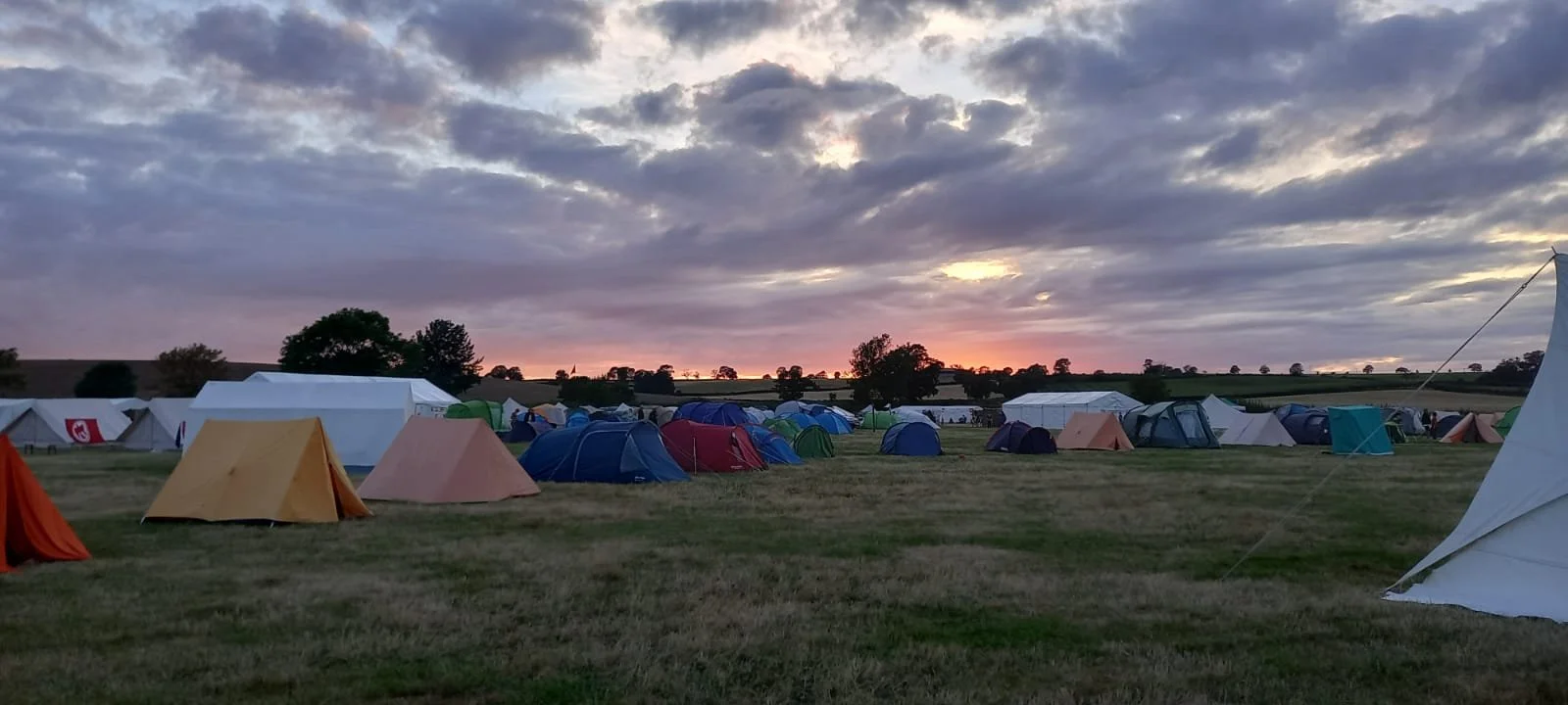 Tents set up on a grassy field at sunset with a cloudy sky.