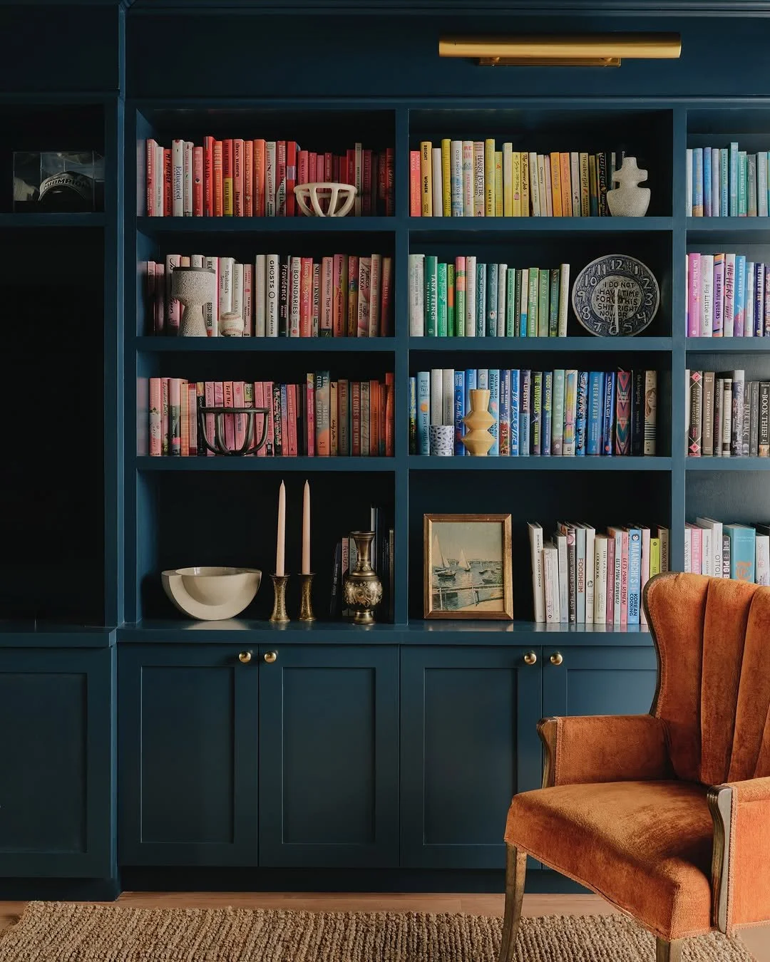 A blue bookshelf filled with colorful books, decorative items, and a framed picture. An orange armchair is partially visible in the foreground.