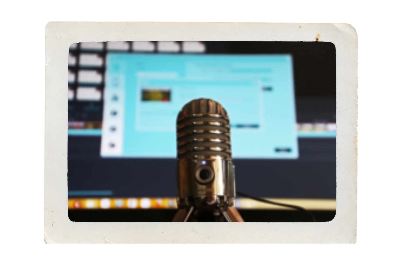 A vintage microphone in front of a computer monitor displaying a social media page, on a table with a blurred background.