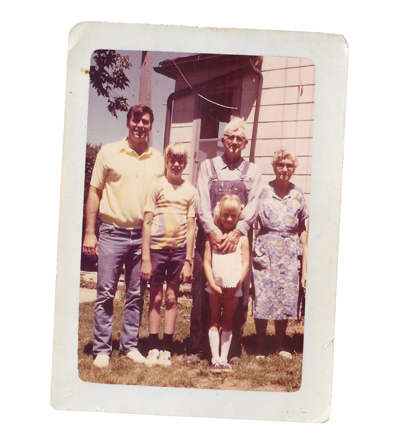 A vintage color photograph of six people standing outdoors in front of a house. Four adults and two children. The adults include a man in a yellow shirt, an older woman with glasses and light hair, another woman with glasses and a floral dress, and a young girl. The children are a boy with blond hair wearing a striped shirt and shorts, and a girl with blond hair in a white dress.