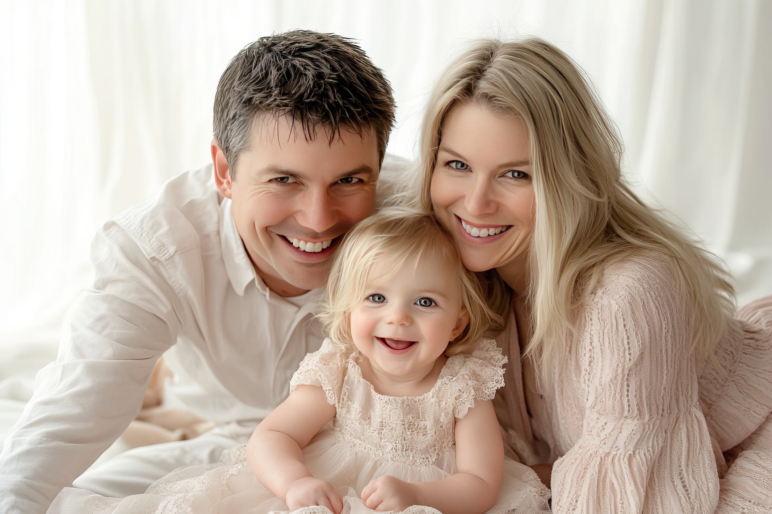 A happy family of three, including a man, woman, and young girl, smiling and lying close together outdoors.