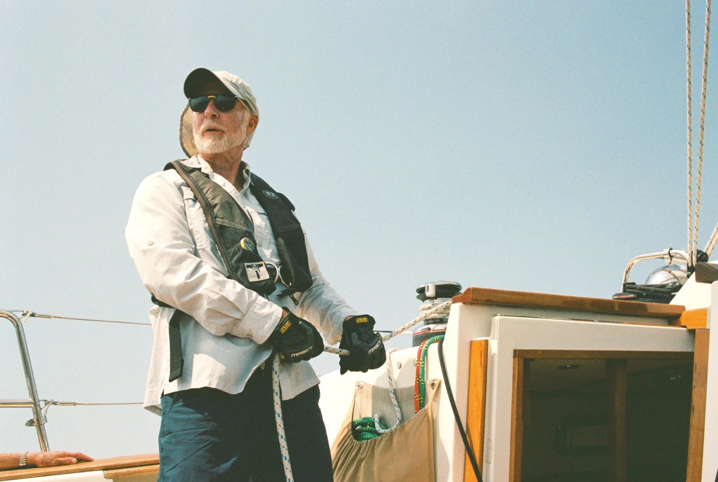 older male sailor focused and serious wearing a life vest and hat and sunglasses sailing a 40 foot sailboat across lake simcoe in jacksons point canada. vintage 35 mm film