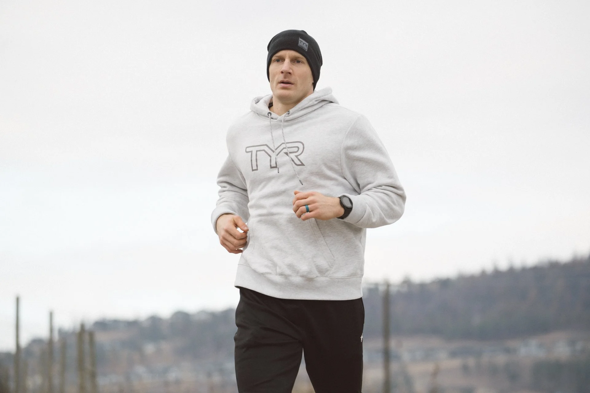 TYR sponsored professional athlete jogging wearing garmin watch and hoodie outside natural light
