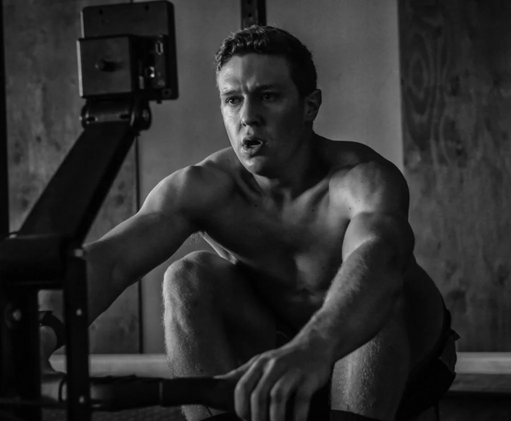 environmental portrait athletic man in black and white with moody window lighting to create shadow. Muscular athlete on rowing machine