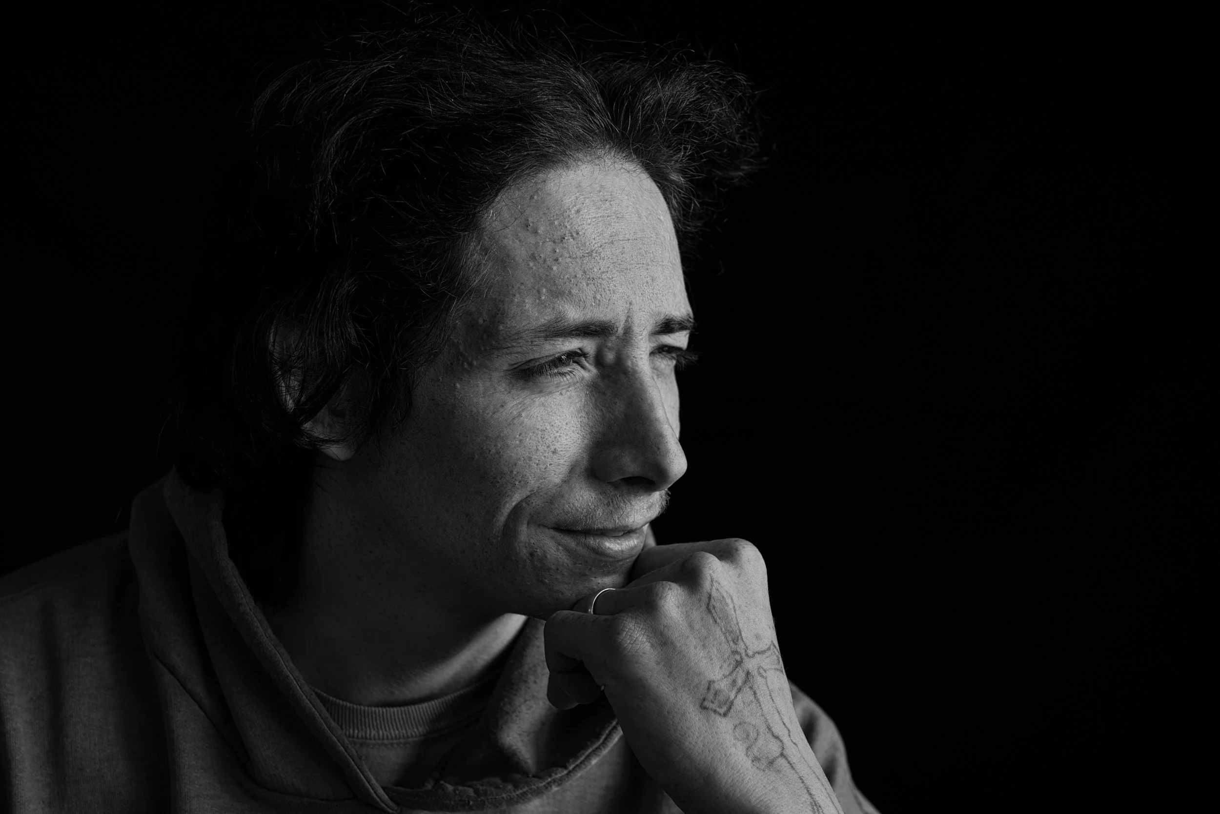 Low key black and white studio light to create mood and shadow of a young man in deep thought with hand tattoo 