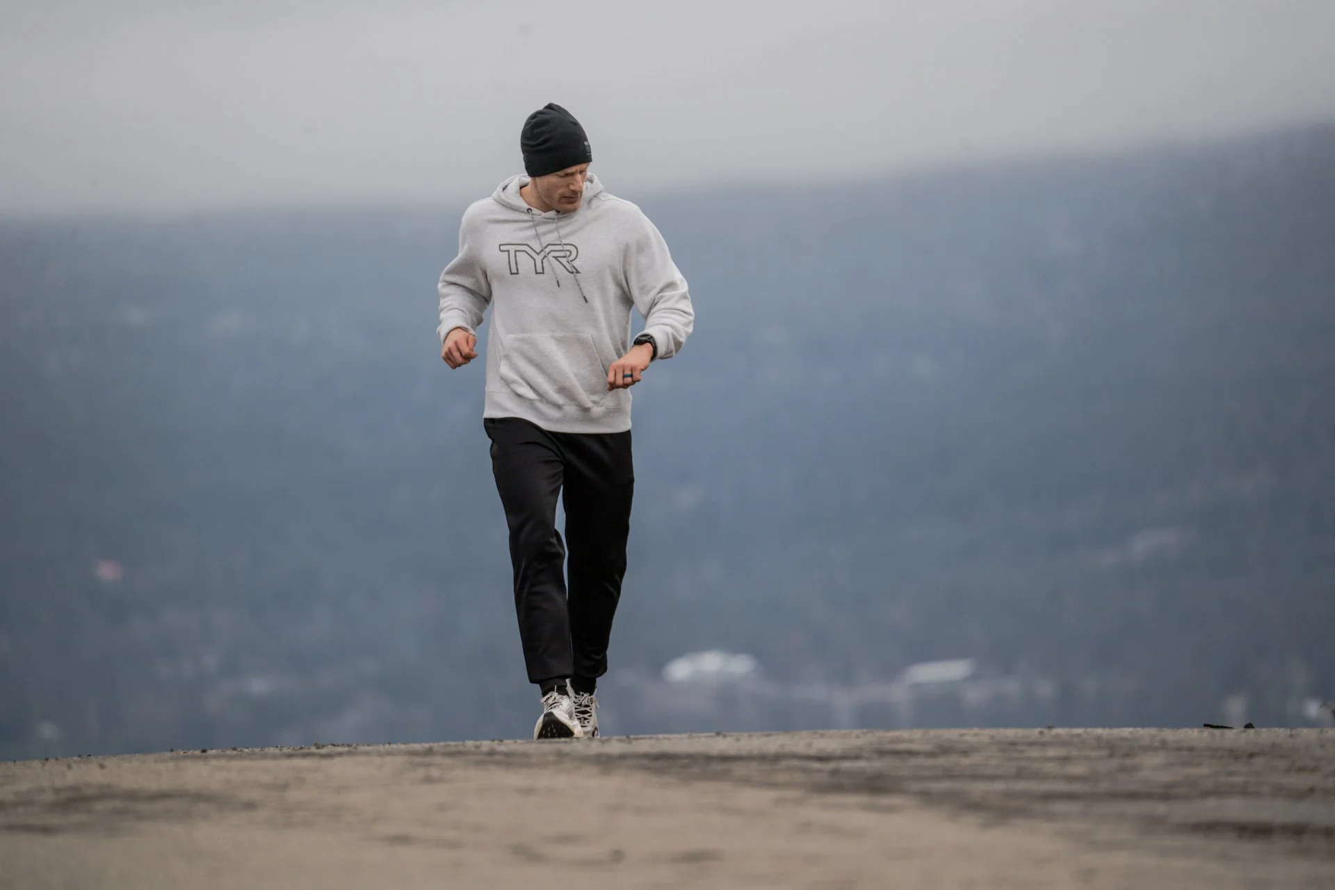 Fit tall man running outside country road. TYR and Garmin sponsored athlete looking at his watch. Outside environmental portrait natural light. 