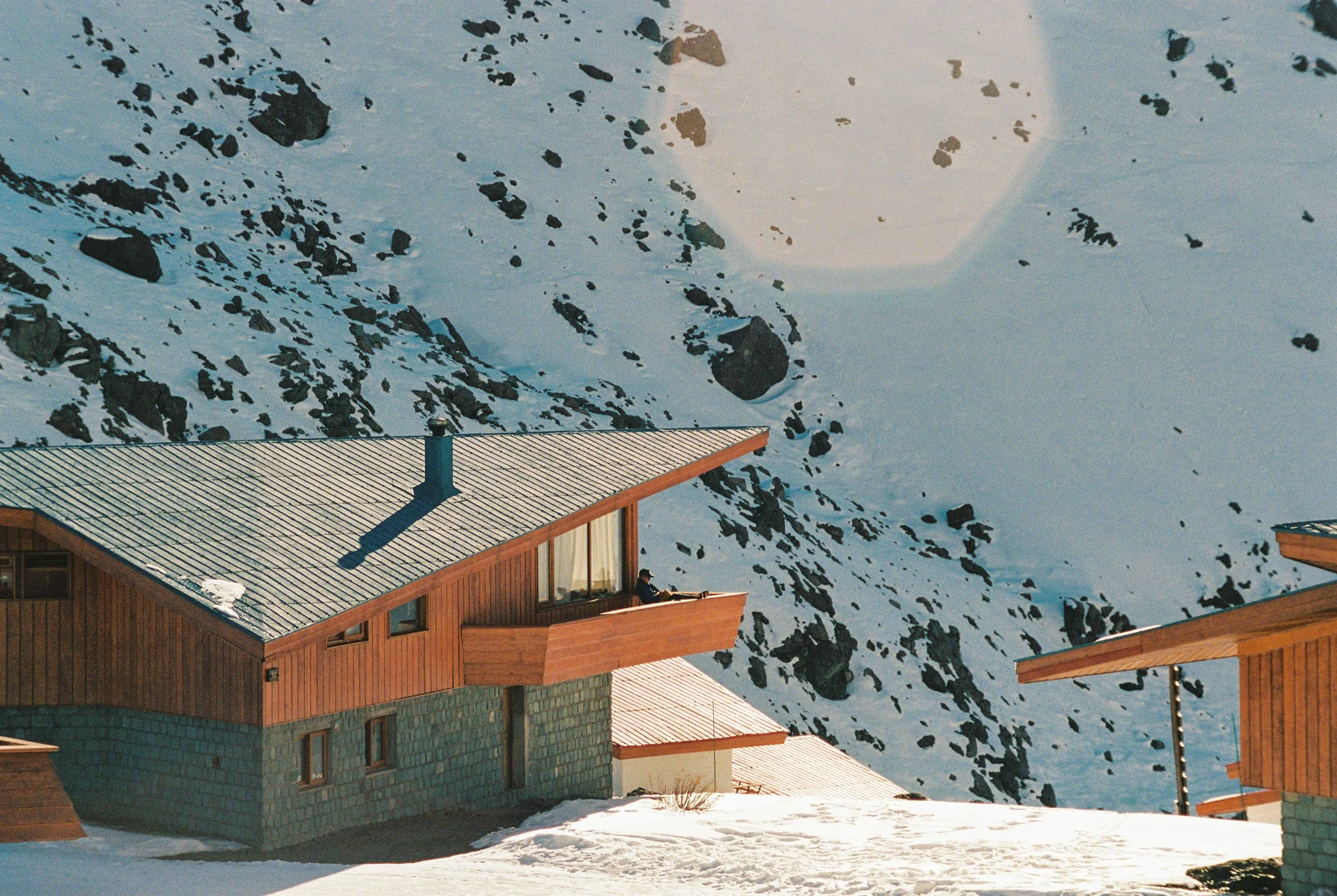 mid century modern design ski chalet in the Andes mountains. man sitting on porch basking in the sun. luxury chalet 35 mm film