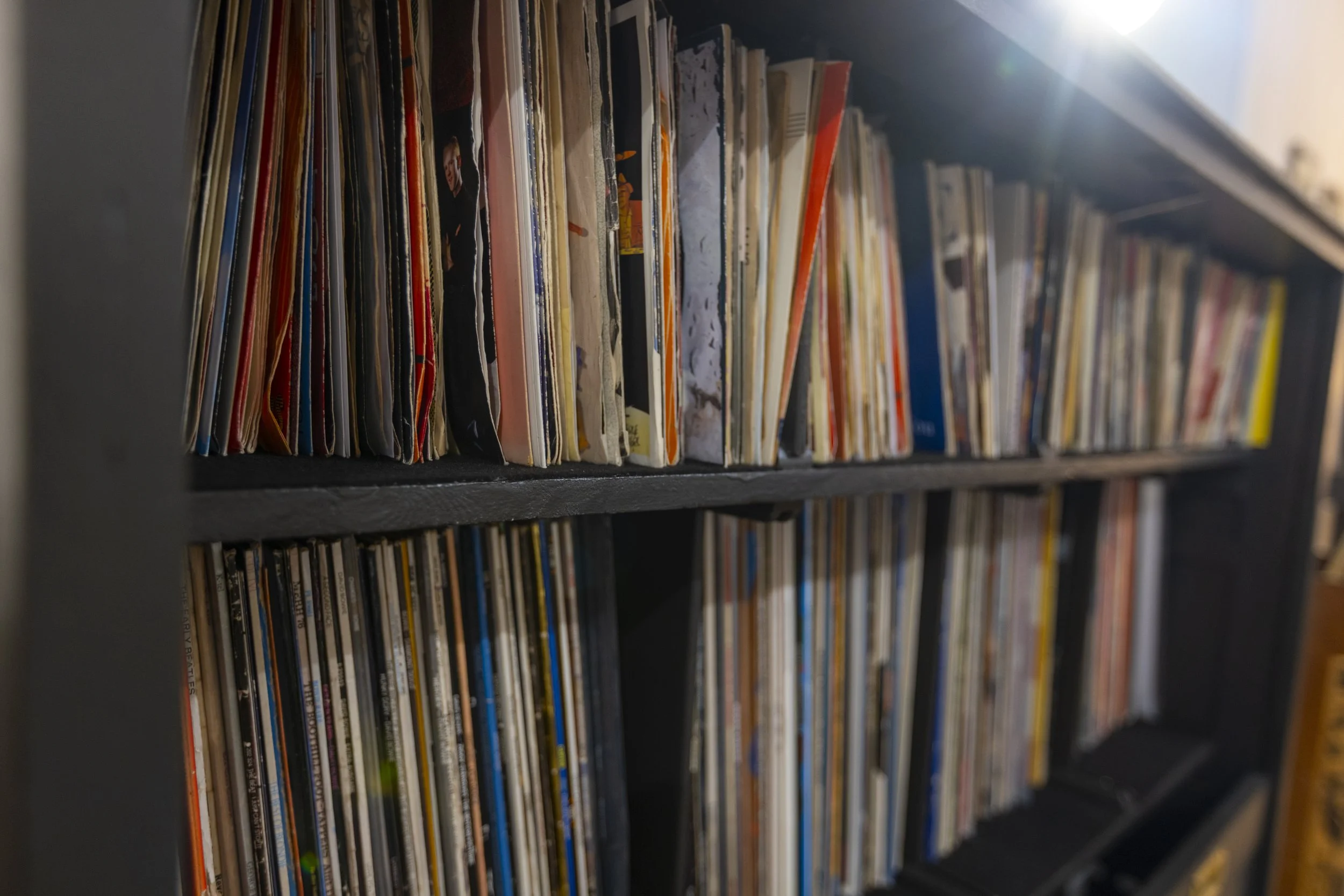 Close-up of a black vinyl record shelf filled with various album covers, some slightly tilted.