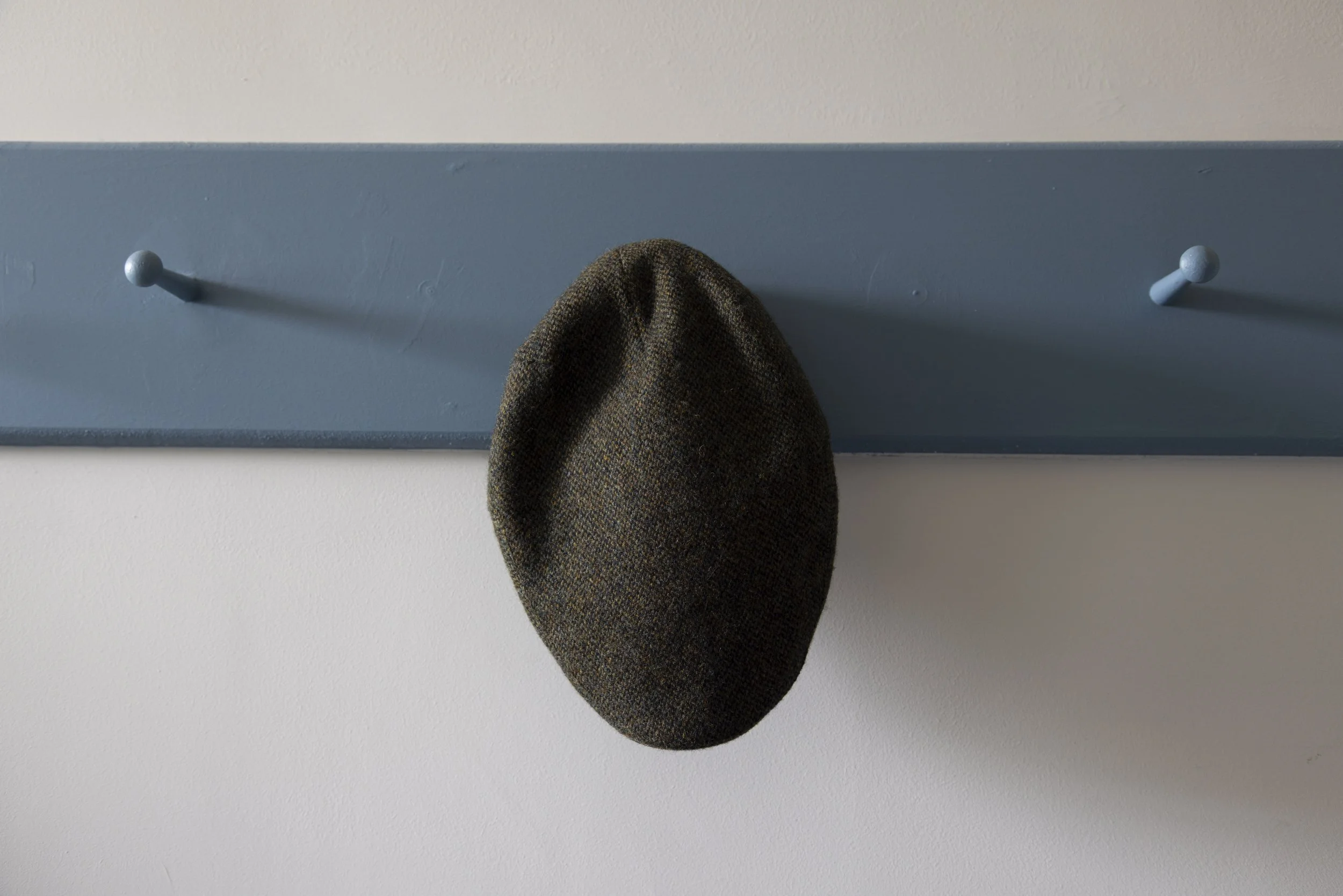 A brown tweed hat hanging on a blue coat rack against a white wall.