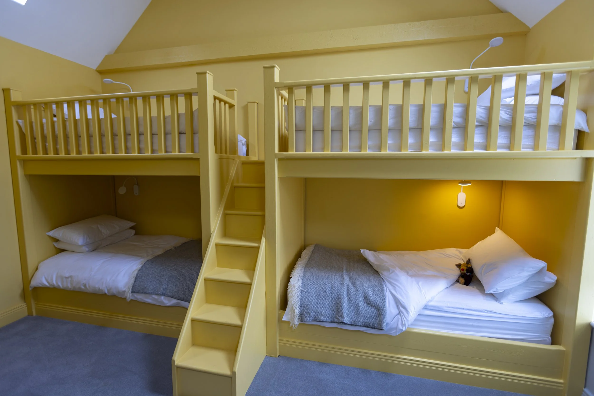 Yellow bunk beds with three sleeping areas, two on the ground level and one on the upper level, in a bedroom with yellow walls and blue carpet.