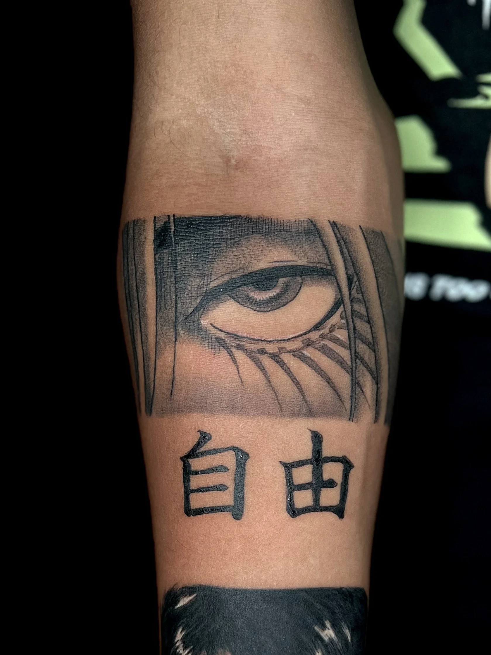 Tattoo of a realistic eye with detailed shading and eyelashes, alongside two Chinese characters meaning 'freedom' or 'liberty'.