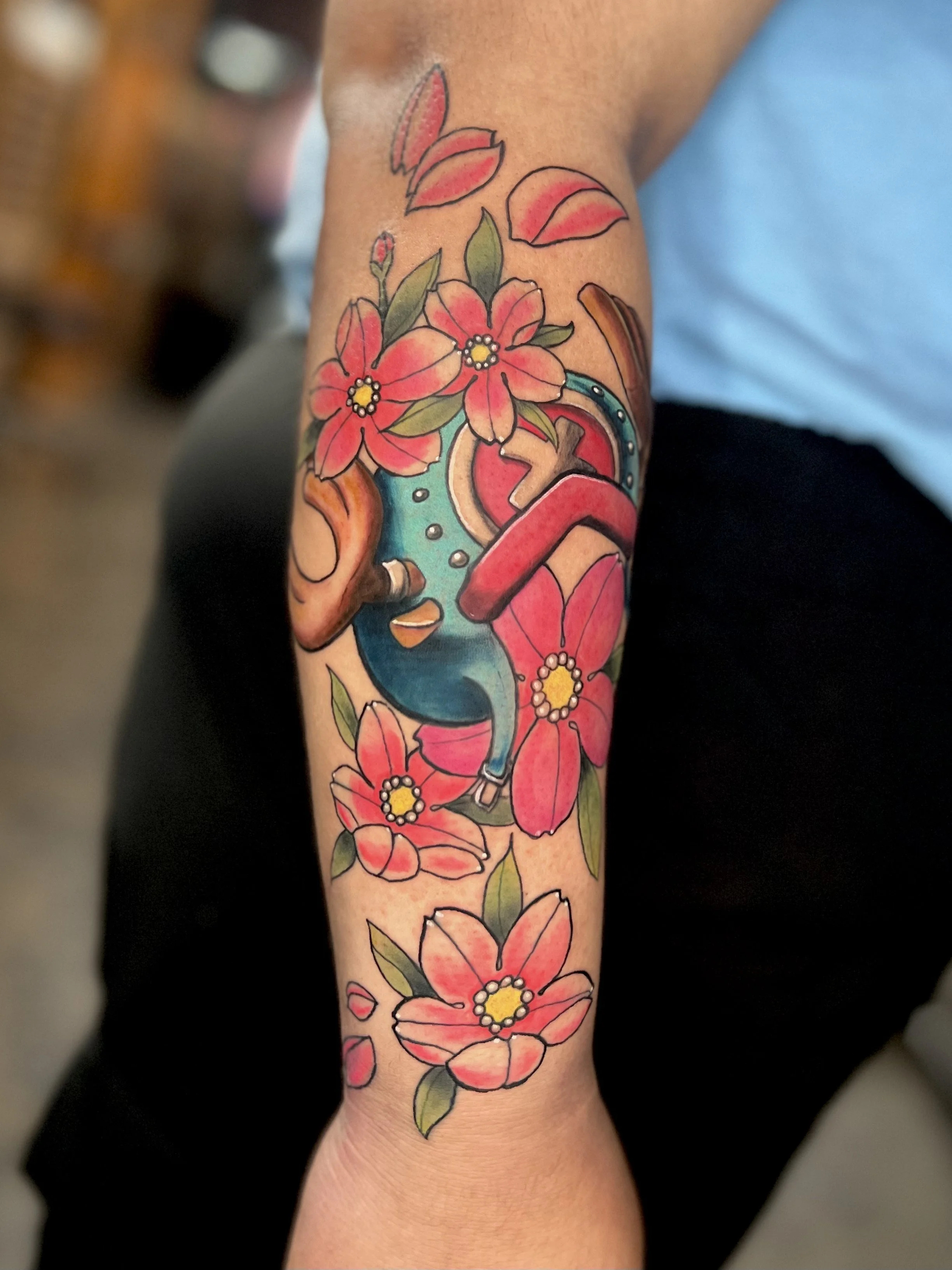 Colorful tattoo of a blue stethoscope intertwined with pink flowers and green leaves on a person's forearm.