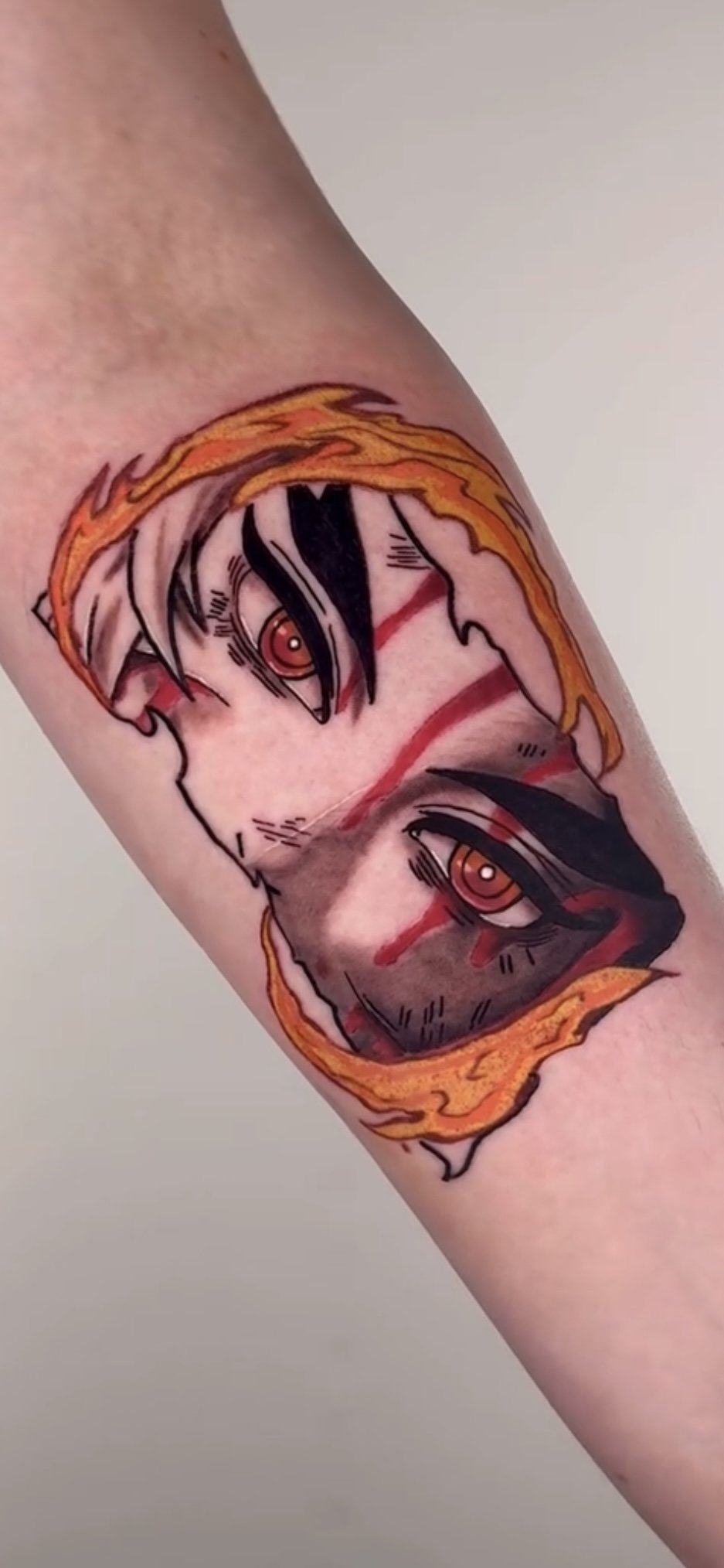 Tattoo of two anime-style faces with red eyes, black hair, and flames surrounding the faces.