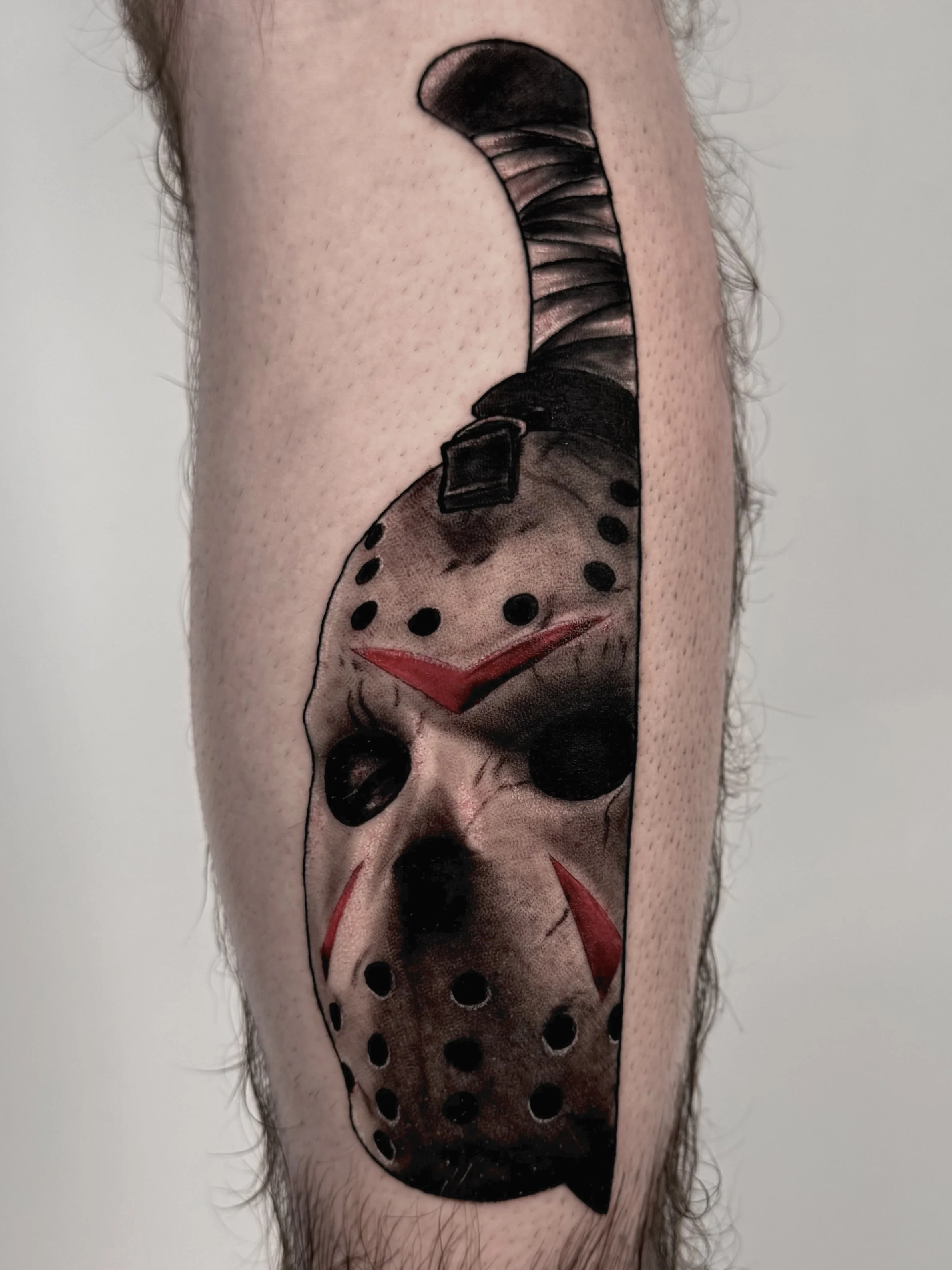 Tattoo of a hockey mask from the horror movie Friday the 13th on a person's arm.