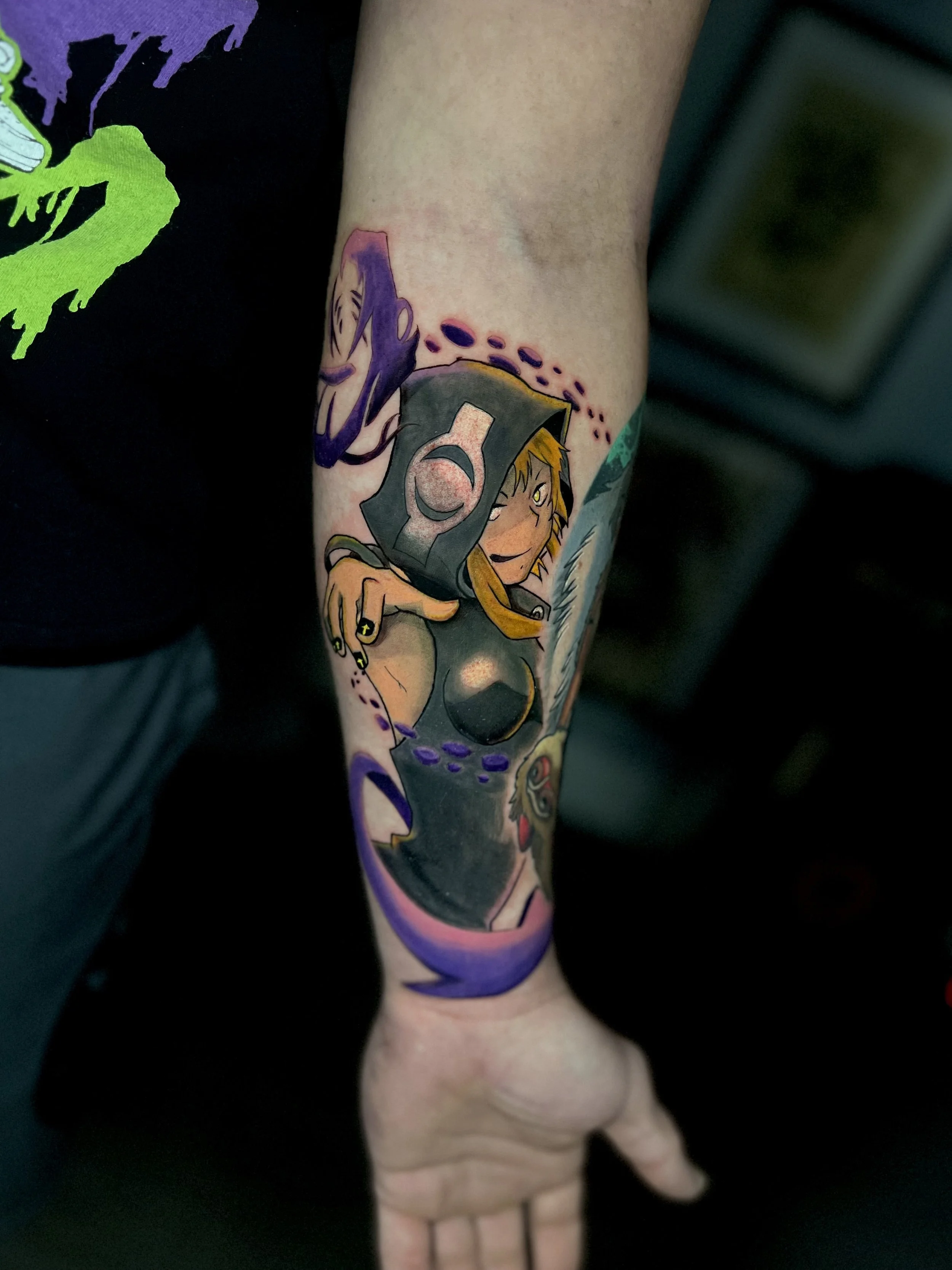 Colorful tattoo of a female character with blonde hair and a dark costume, winking and holding a feather, with purple and other colored accents on the arm.