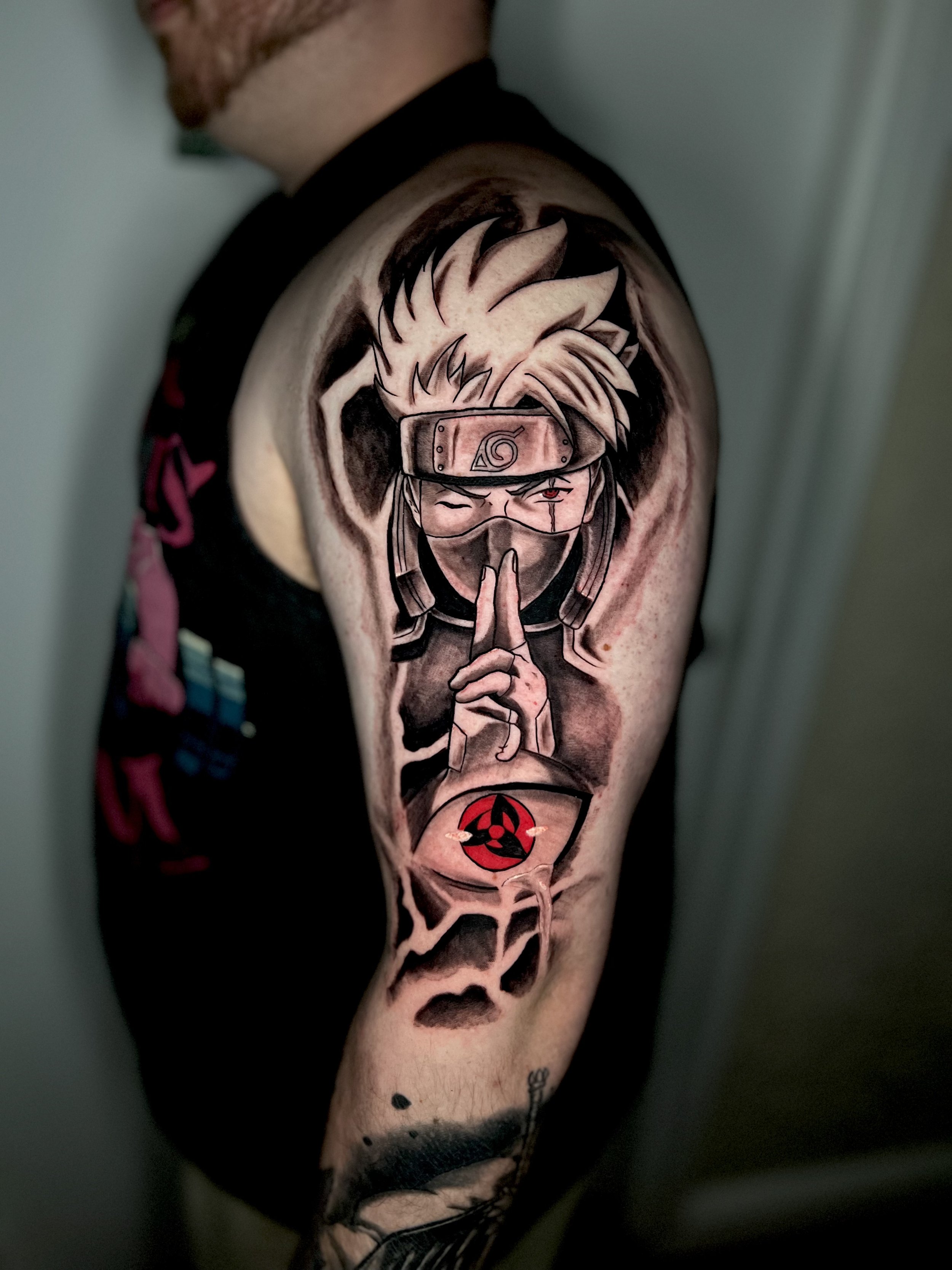 Tattoo of a ninja character with spiky hair, headband, and finger gesture, featuring a red symbol from Naruto on the forearm.