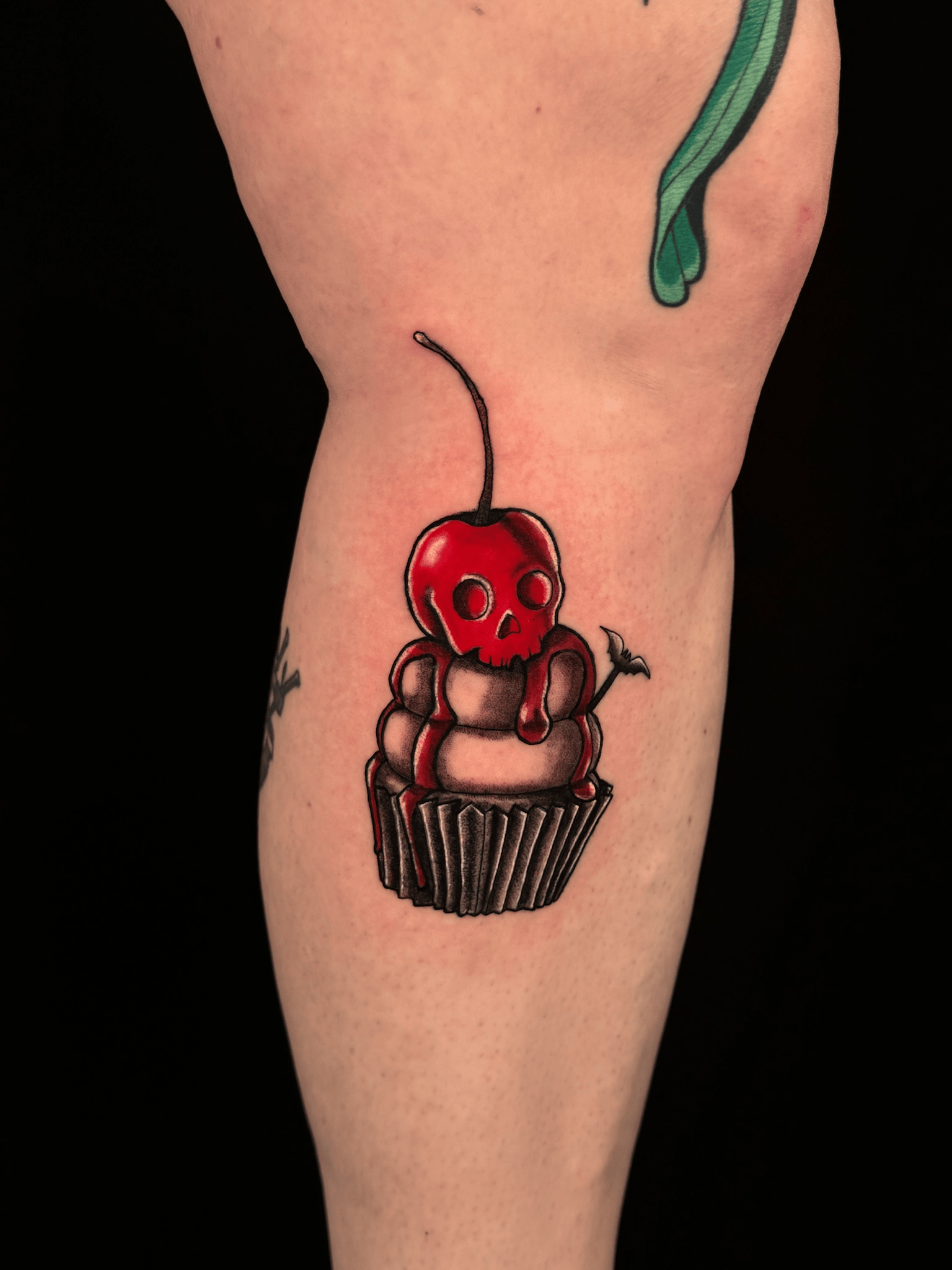 Tattoo of a cherry with a skull face on top of a cupcake.
