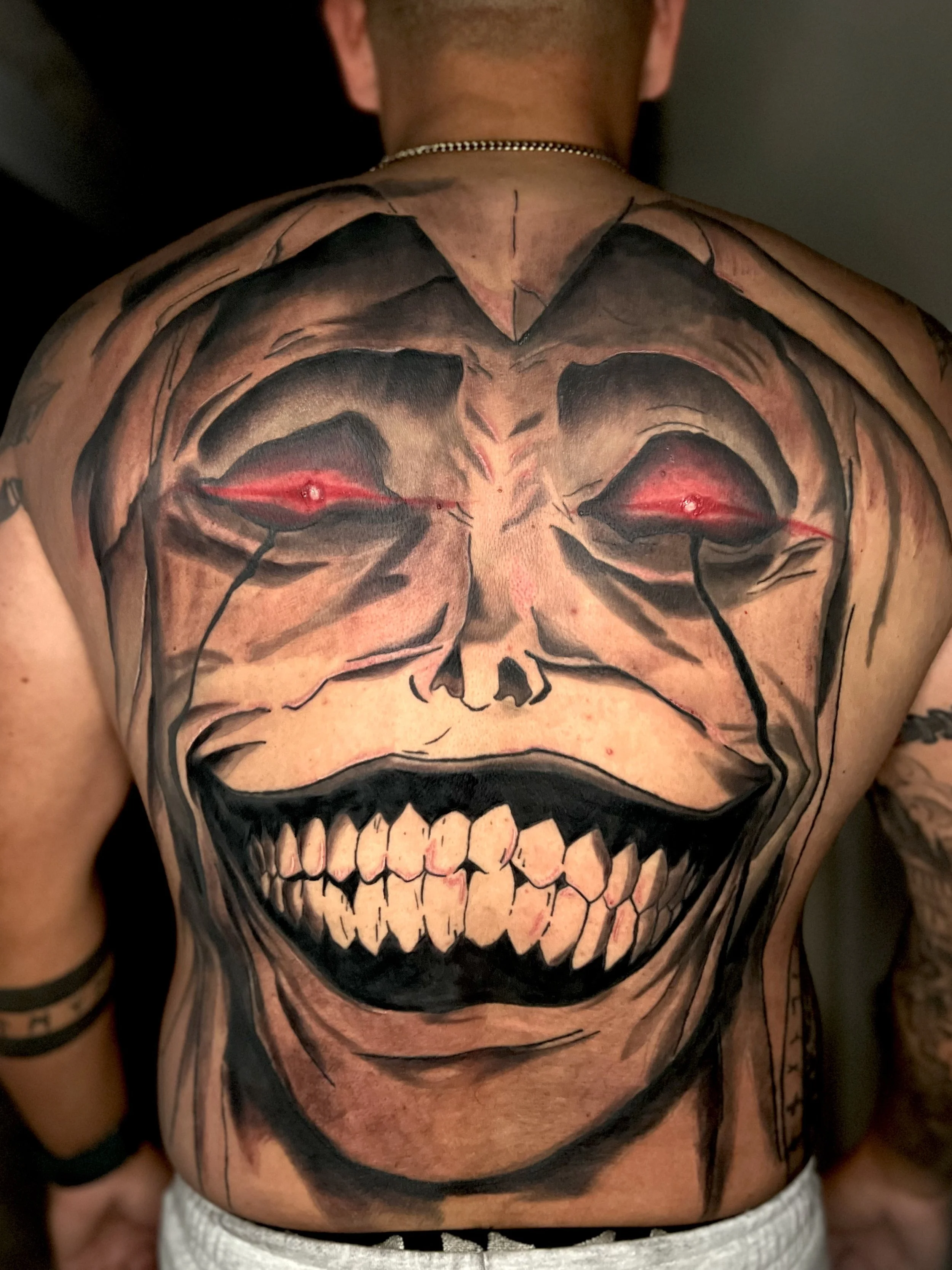 Tattoo of a grinning skull with glowing red eyes on a person's back.