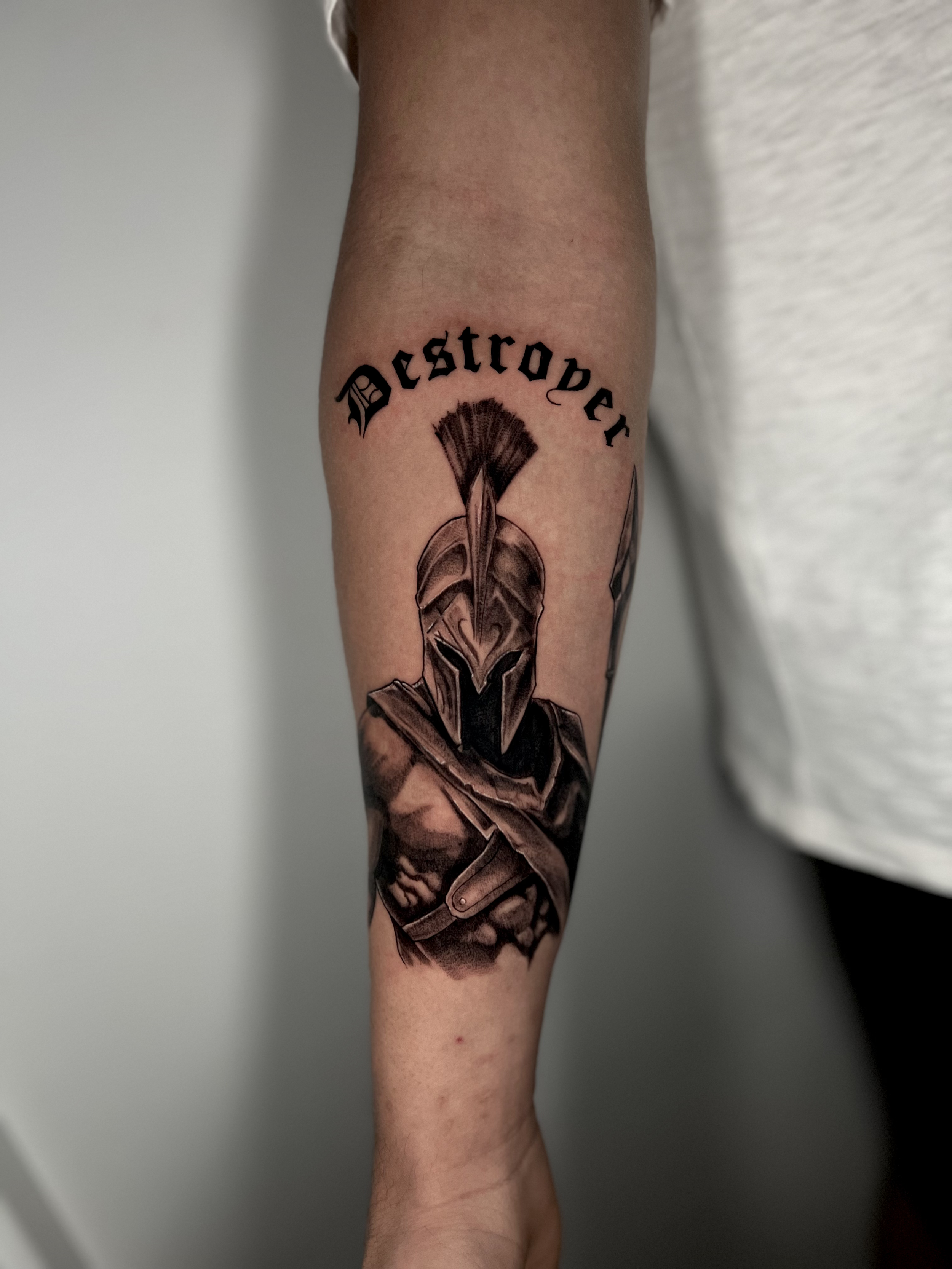 Tattoo of a warrior helmeted soldier with the word 'Deconstructor' above it on a person's forearm
