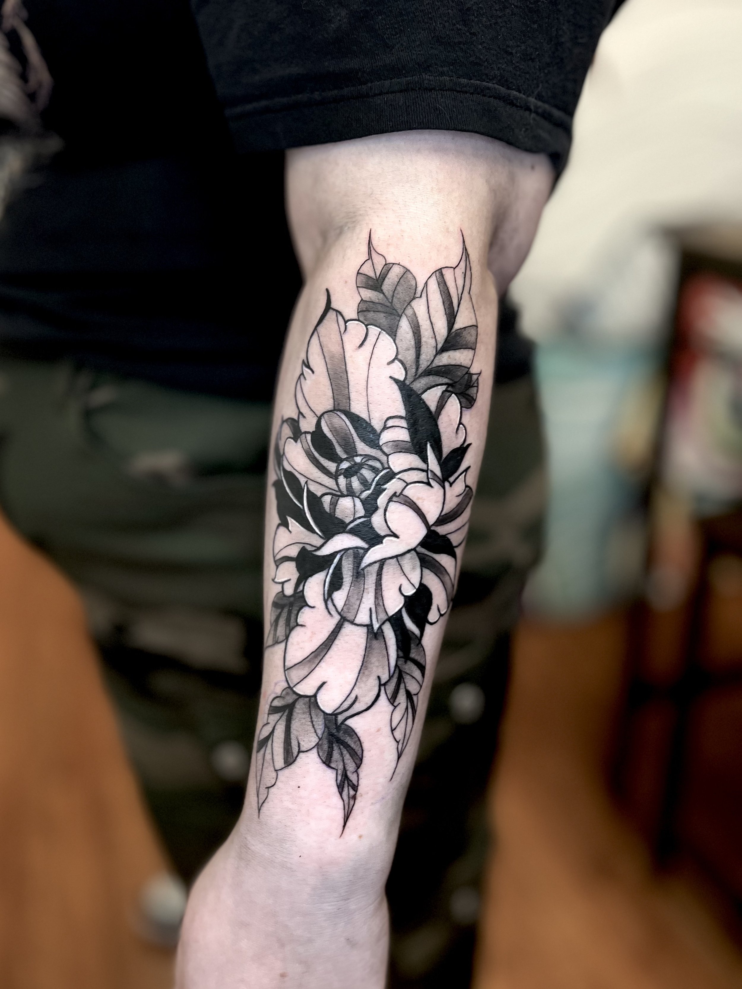 Black and gray floral tattoo on person's forearm, featuring a large blooming flower with leaves.