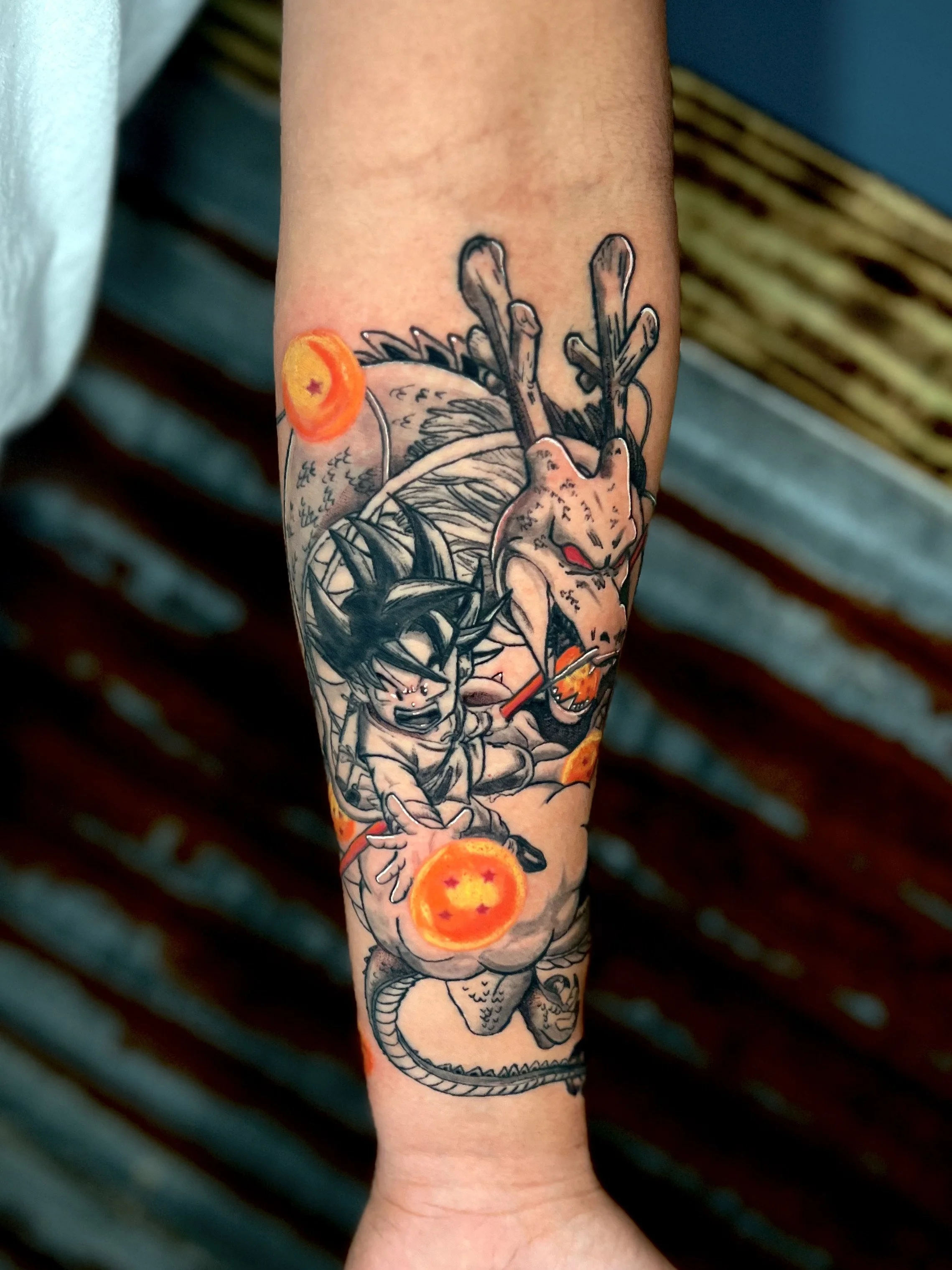Tattoo of Goku and a dragon, with Dragon Balls, on a person's forearm.