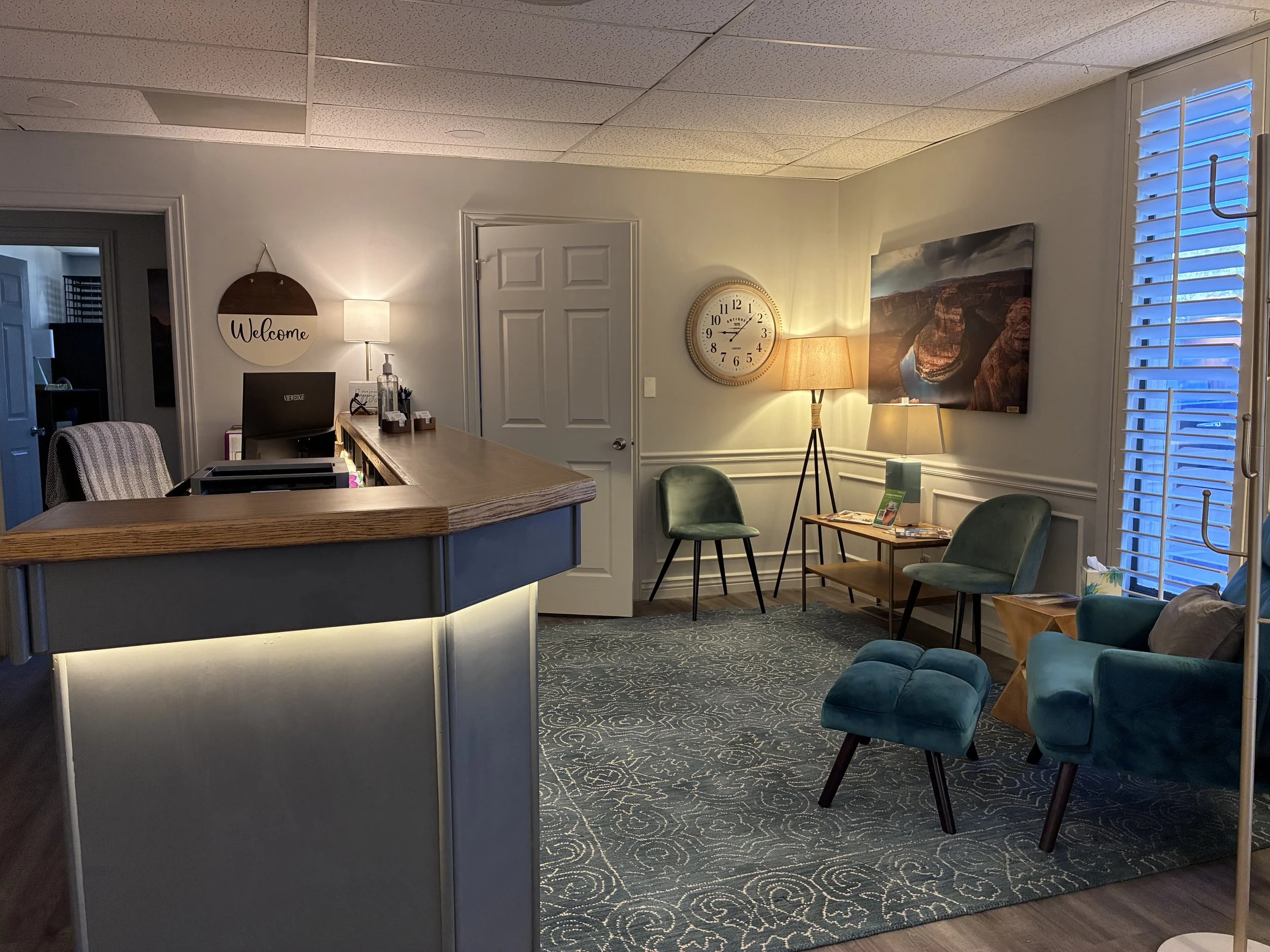 A cozy waiting room with teal chairs, illuminated by soft lighting and a blue-tinted window to create a comfortable waiting room in Ogden Utah for people needing expert psychiatric medication management.