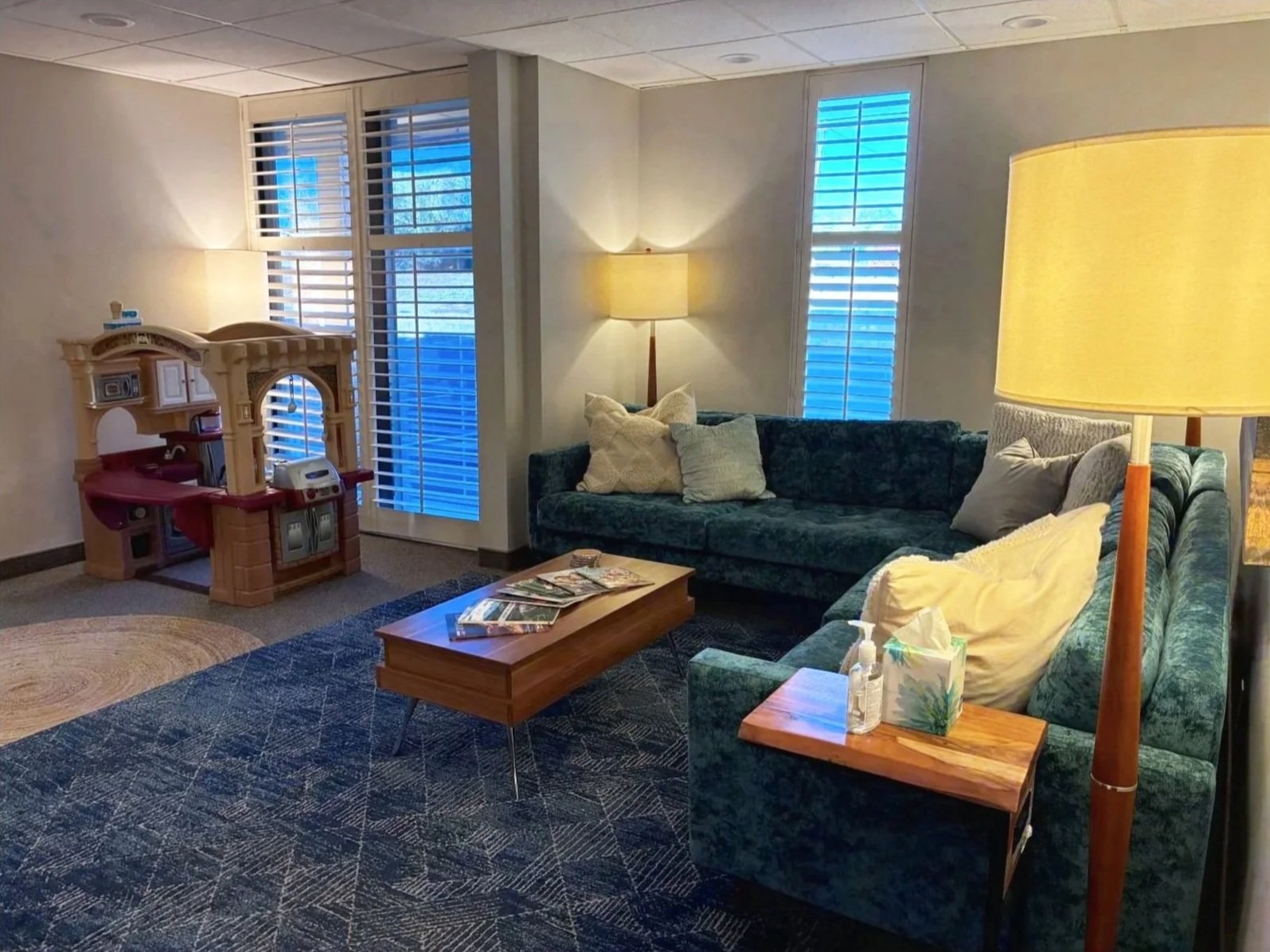 Living room with dark green sofa and play area for kids while families are receiving mental health treatment at Good Day Mental Health in Ogden Utah