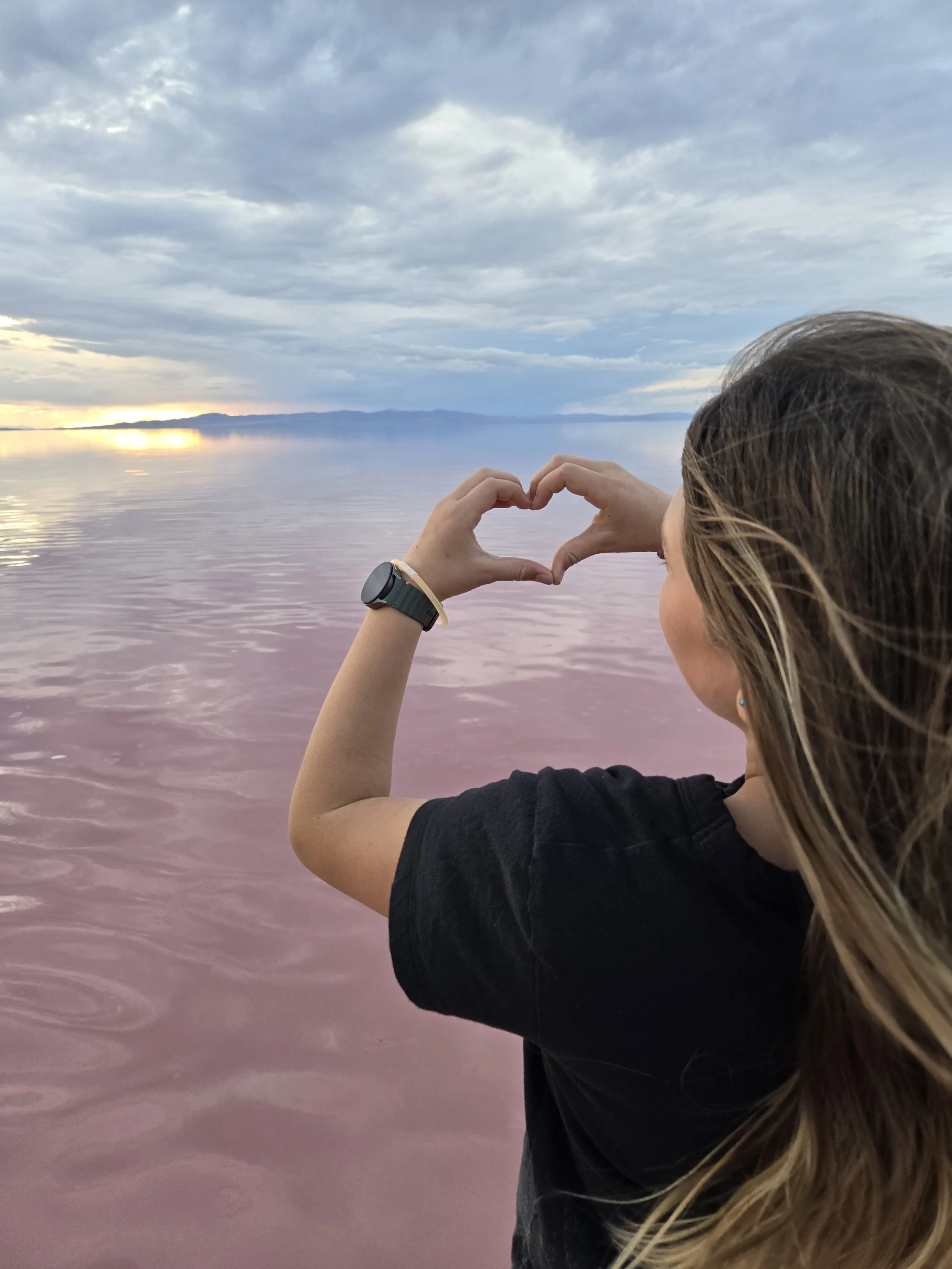 A healthy teenage girl makes hearts at the sunset at the Great Salt Lake after psychiatric treatment at Good Day Psychiatry
