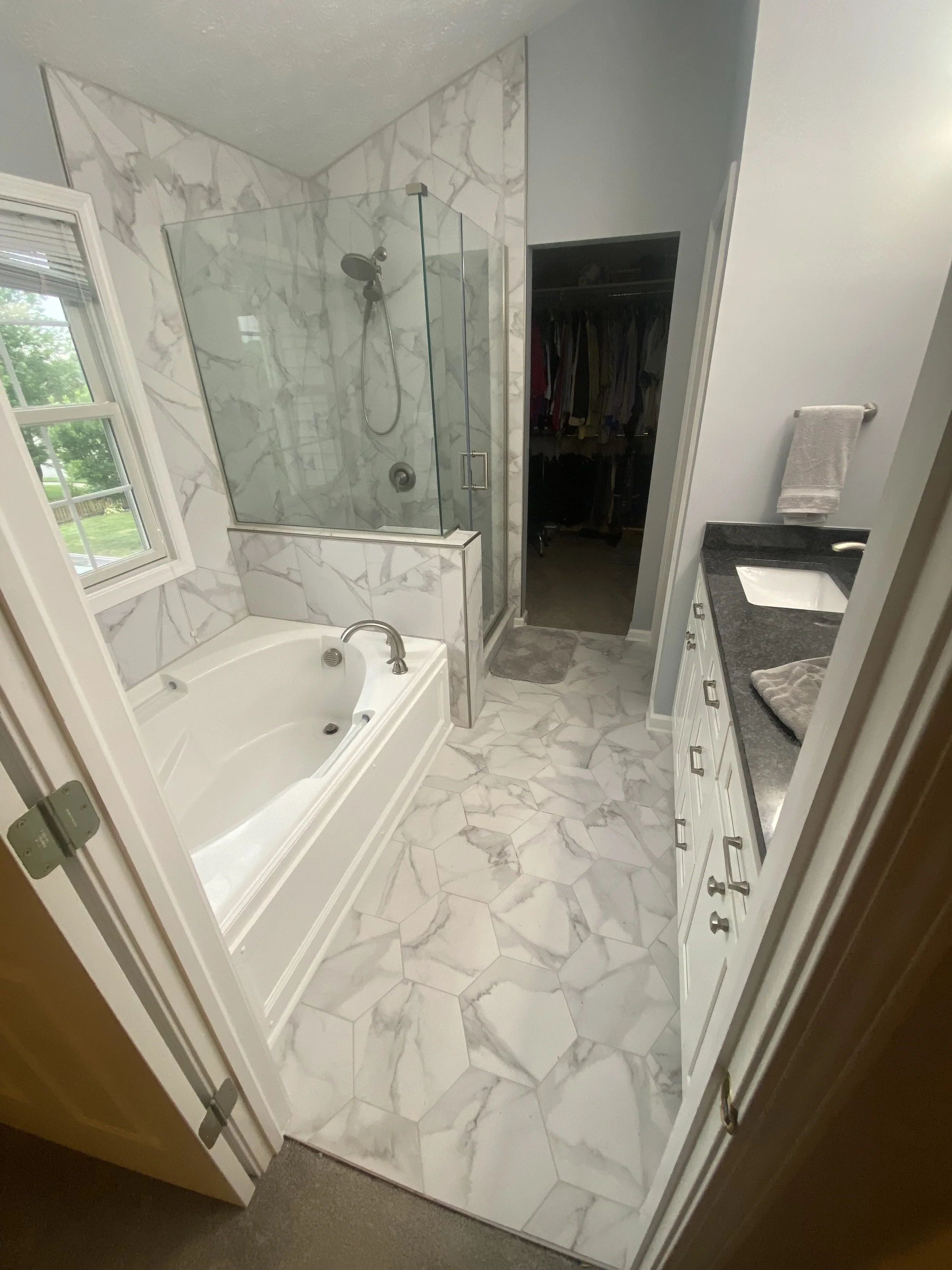 Bathroom with a bathtub, a glass-enclosed shower, a window, a vanity with a sink, and an open closet.