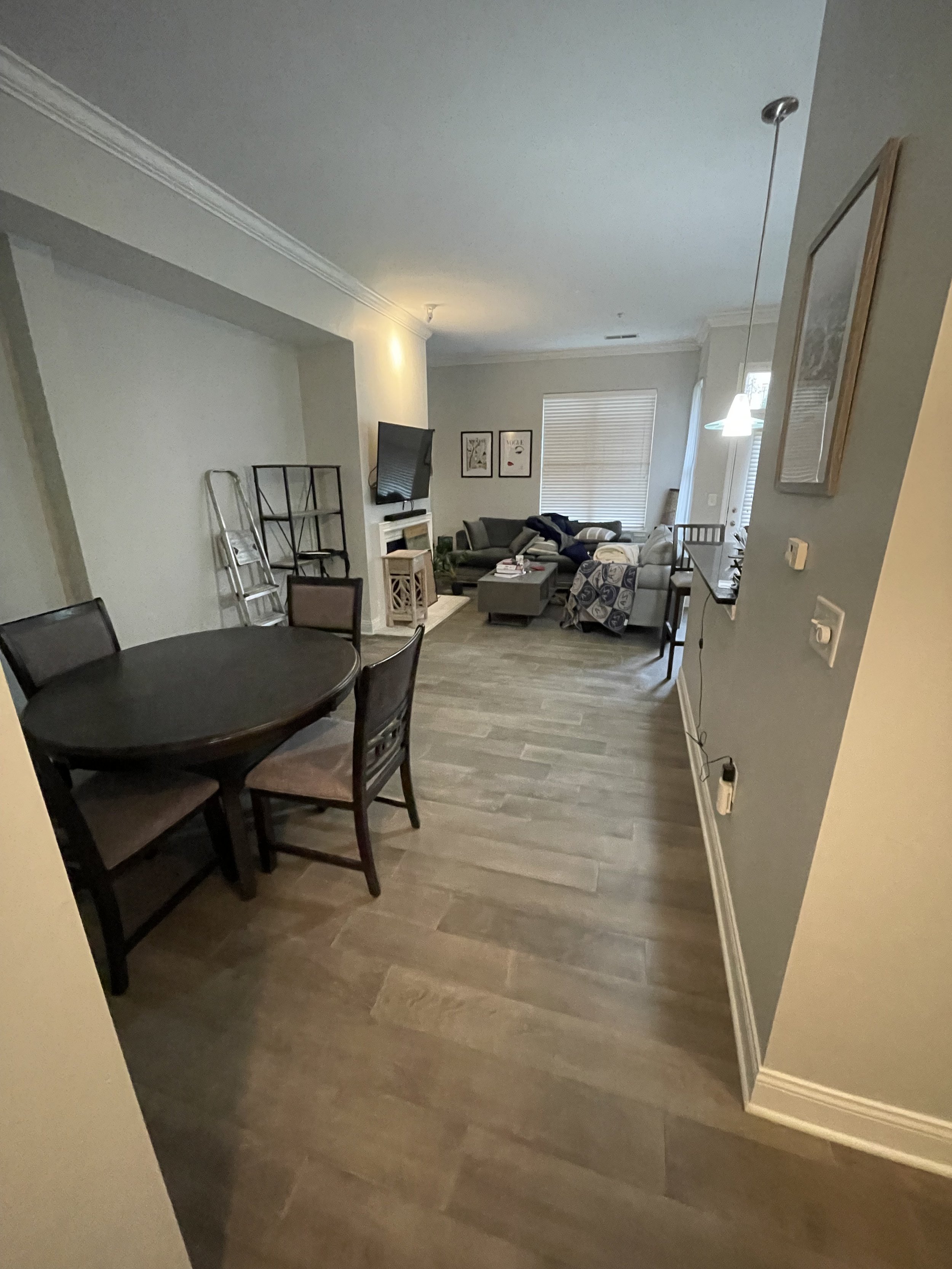 A living room and dining area with wooden flooring, a round dining table with four chairs, a sitting area with couches, a TV on a wall mount, and wall art.