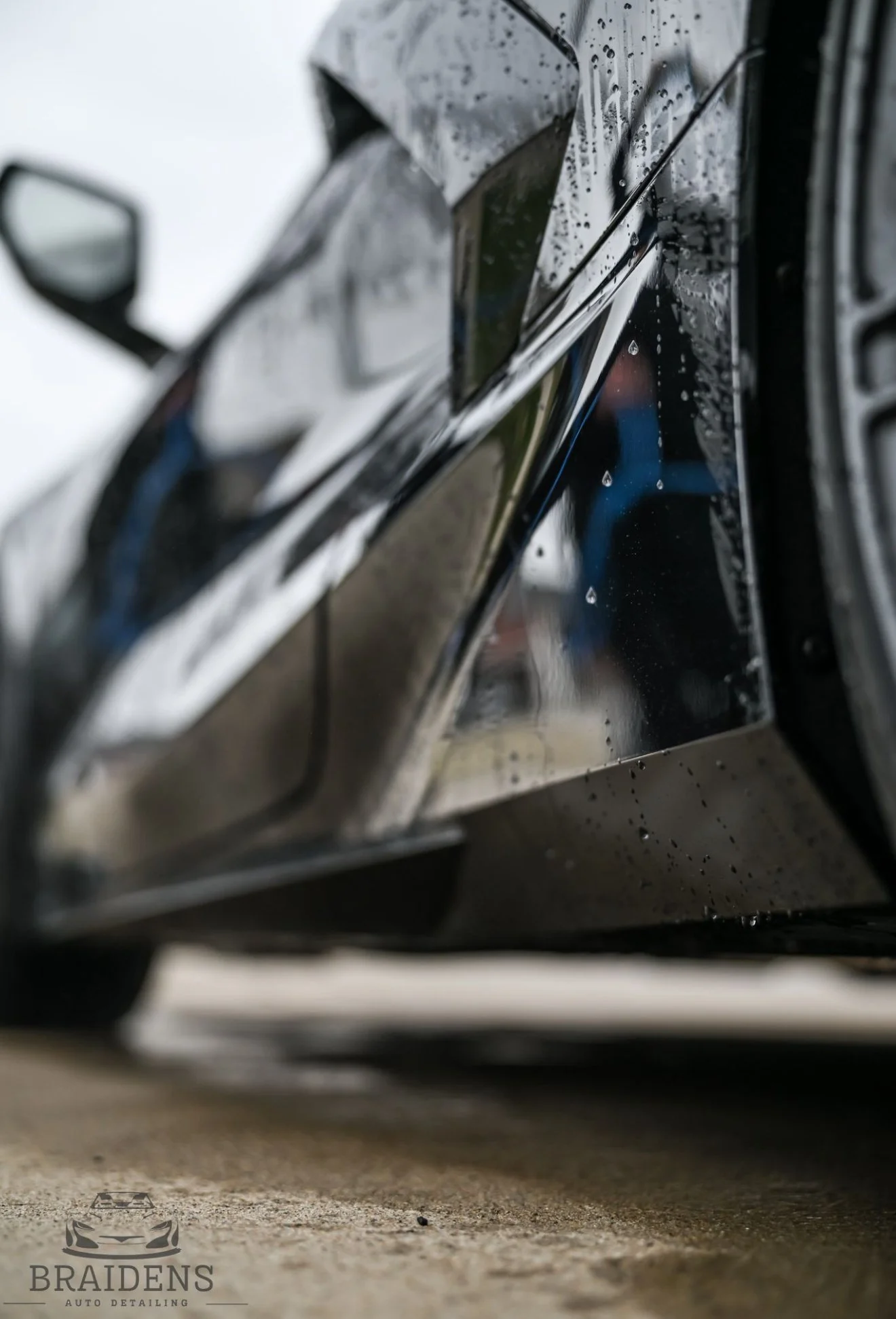 Close-up of a black car with rain droplets on its surface, viewed from a low angle.