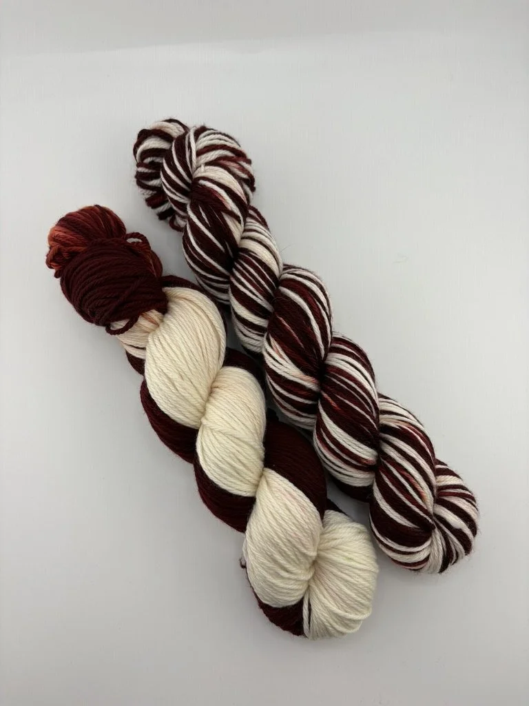 2 Hand‑dyed yarn skeins in white and maroon shades arranged together.”