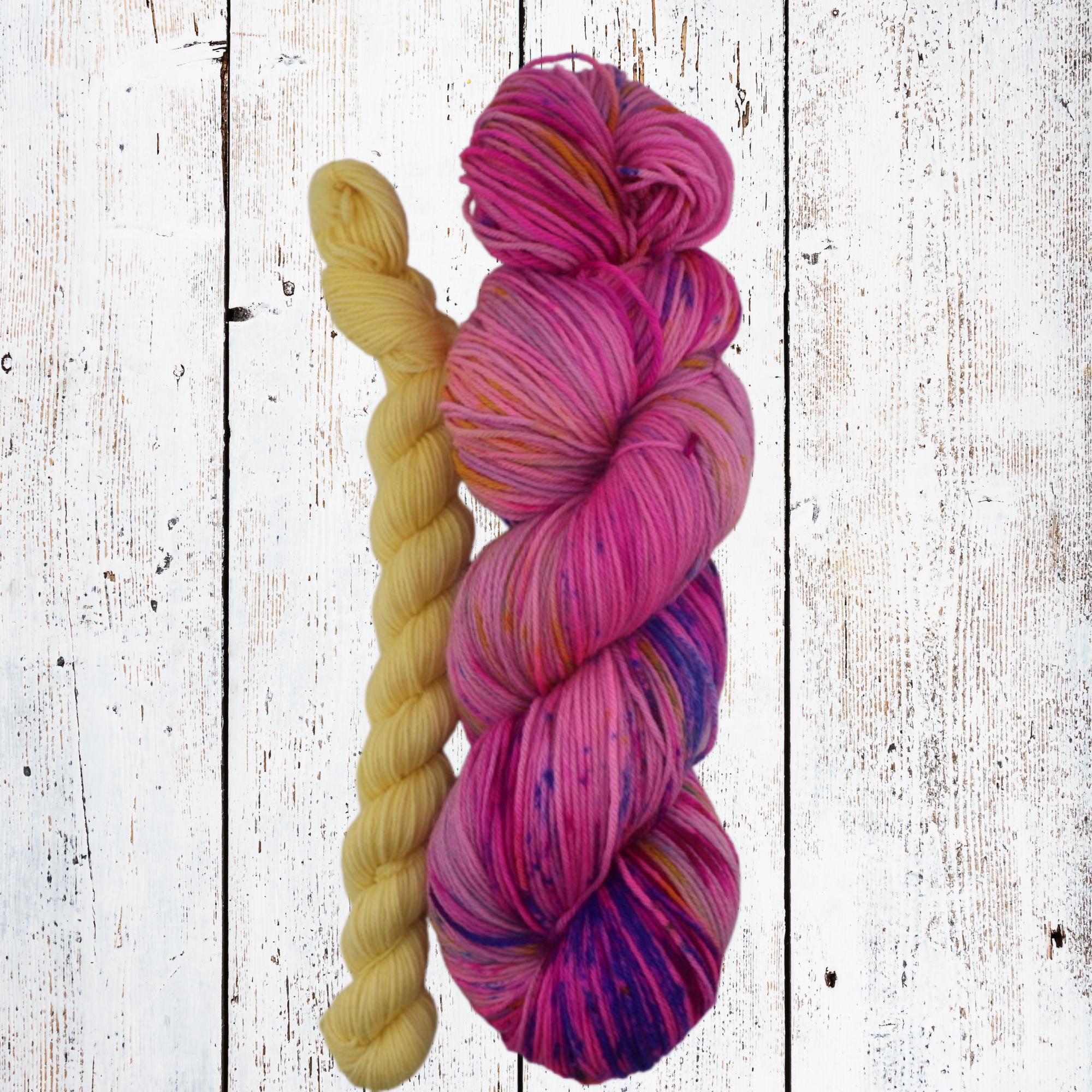 Bright pink, purple and magenta yarn skeins with a single yellow skein, styled in a woven basket on a white wooden background to highlight bold colour contrast and fibre texture.