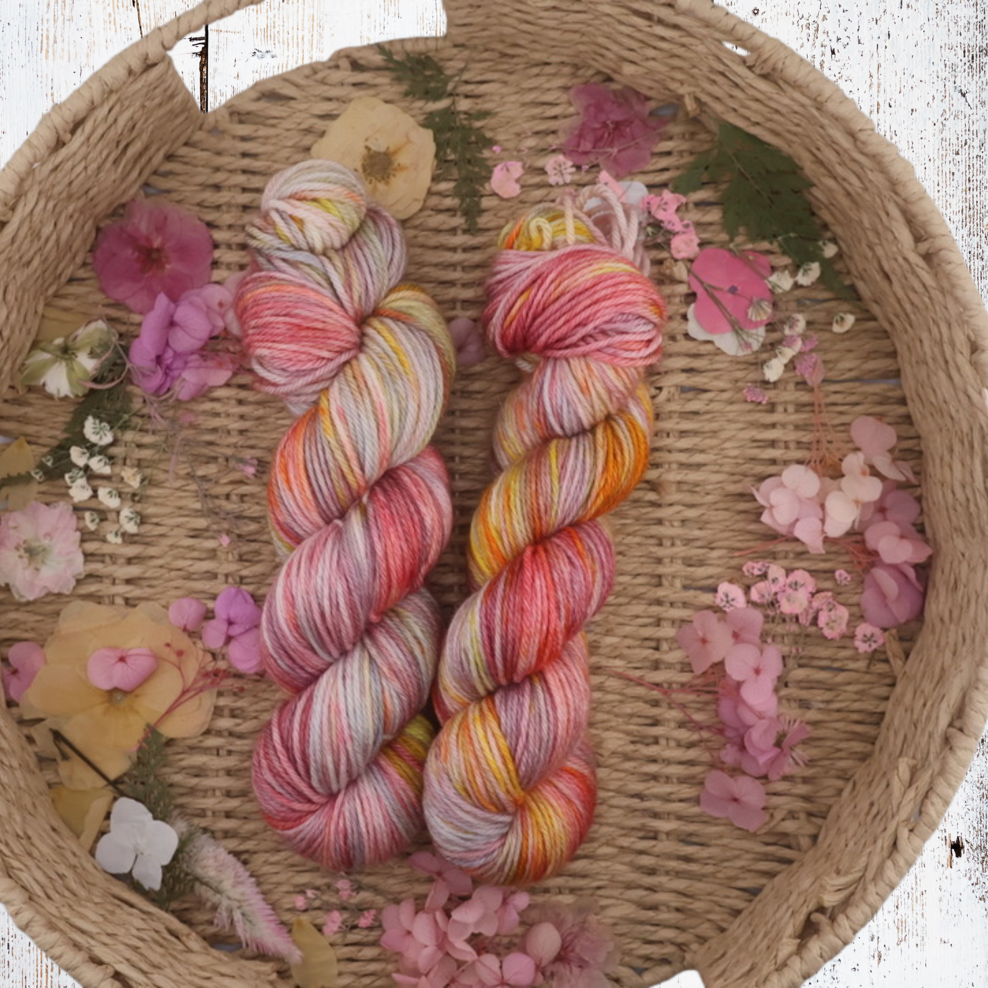 Close‑up of vibrant pink, orange, yellow and purple hand‑dyed yarn skeins arranged in a basket, highlighting the smooth twist and colour transitions