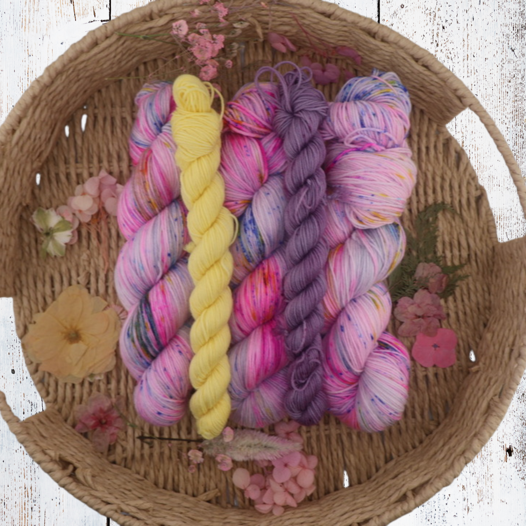 Pastel and vibrant yarn skeins in pink, purple, blue and yellow arranged in a woven basket, showcasing tonal blends and soft halo on a white background.