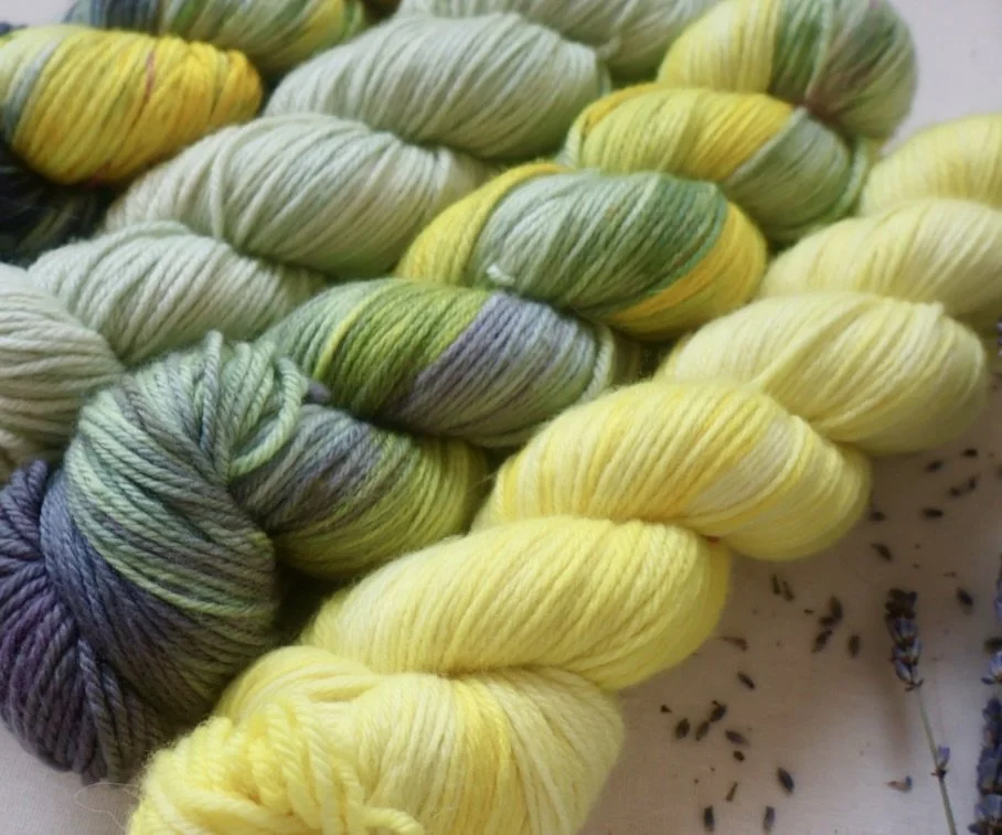 Textured grouping of the Queen’s Attendant hand‑dyed yarn set, highlighting the blend of charcoal, moss green, and vibrant yellow tones.