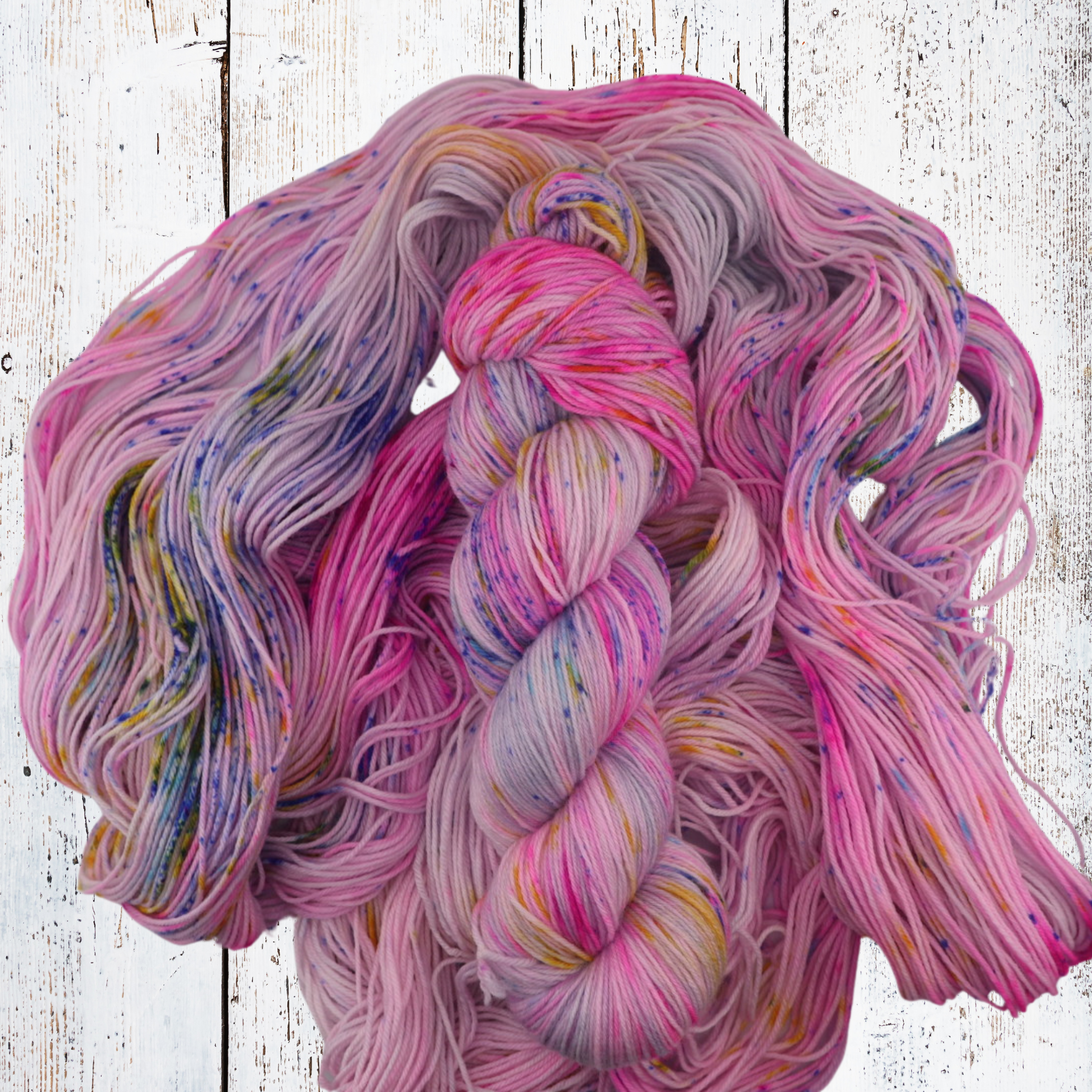 Loose hand‑dyed yarn in teal, blue and purple shades arranged on a white wooden surface to highlight tonal variation and fibre texture.