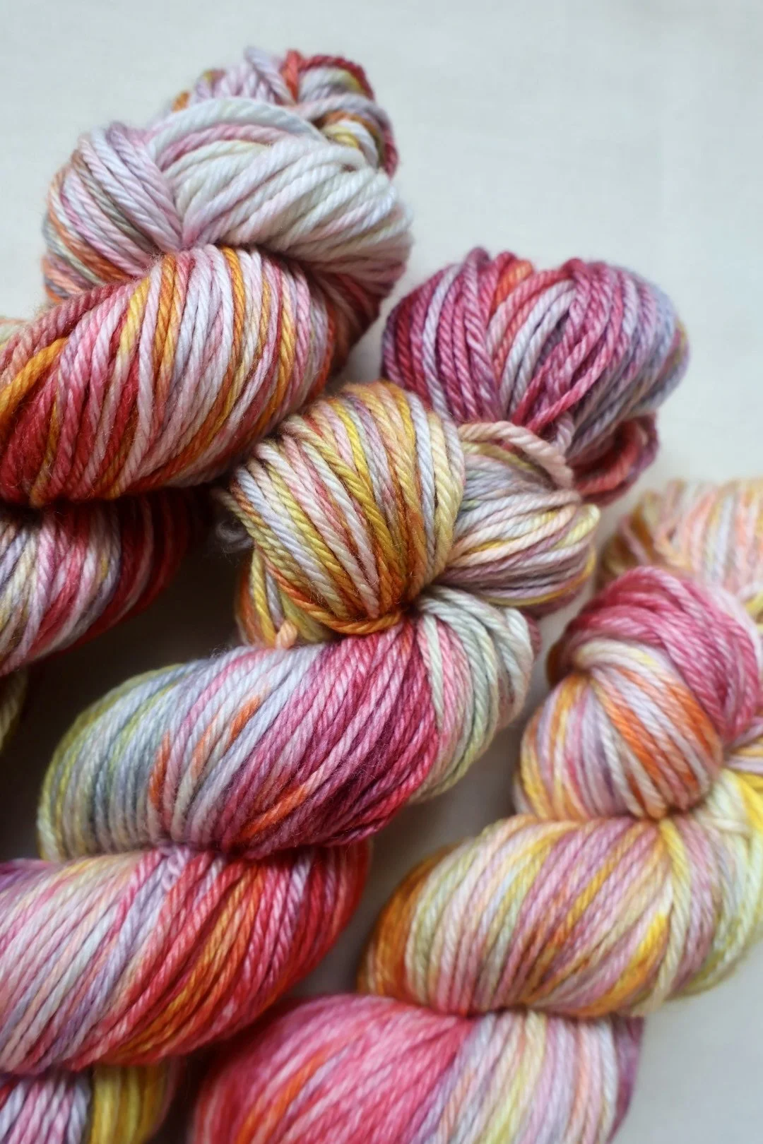 Variegated merino yarn skeins featuring warm pink, coral, gold, and grey shades, hand dyed in Scotland