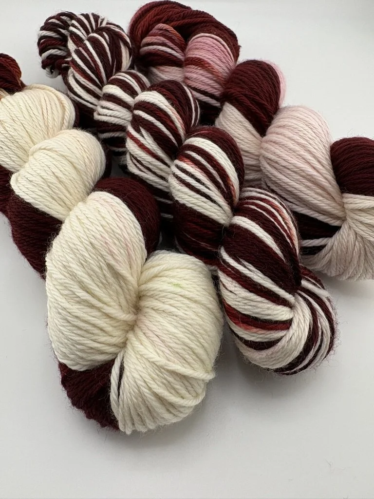 Hand‑dyed yarn skeins in maroon and white arranged together.”