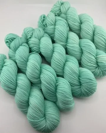 Hand‑dyed yarn skeins in mint green shades arranged in a neat pile.