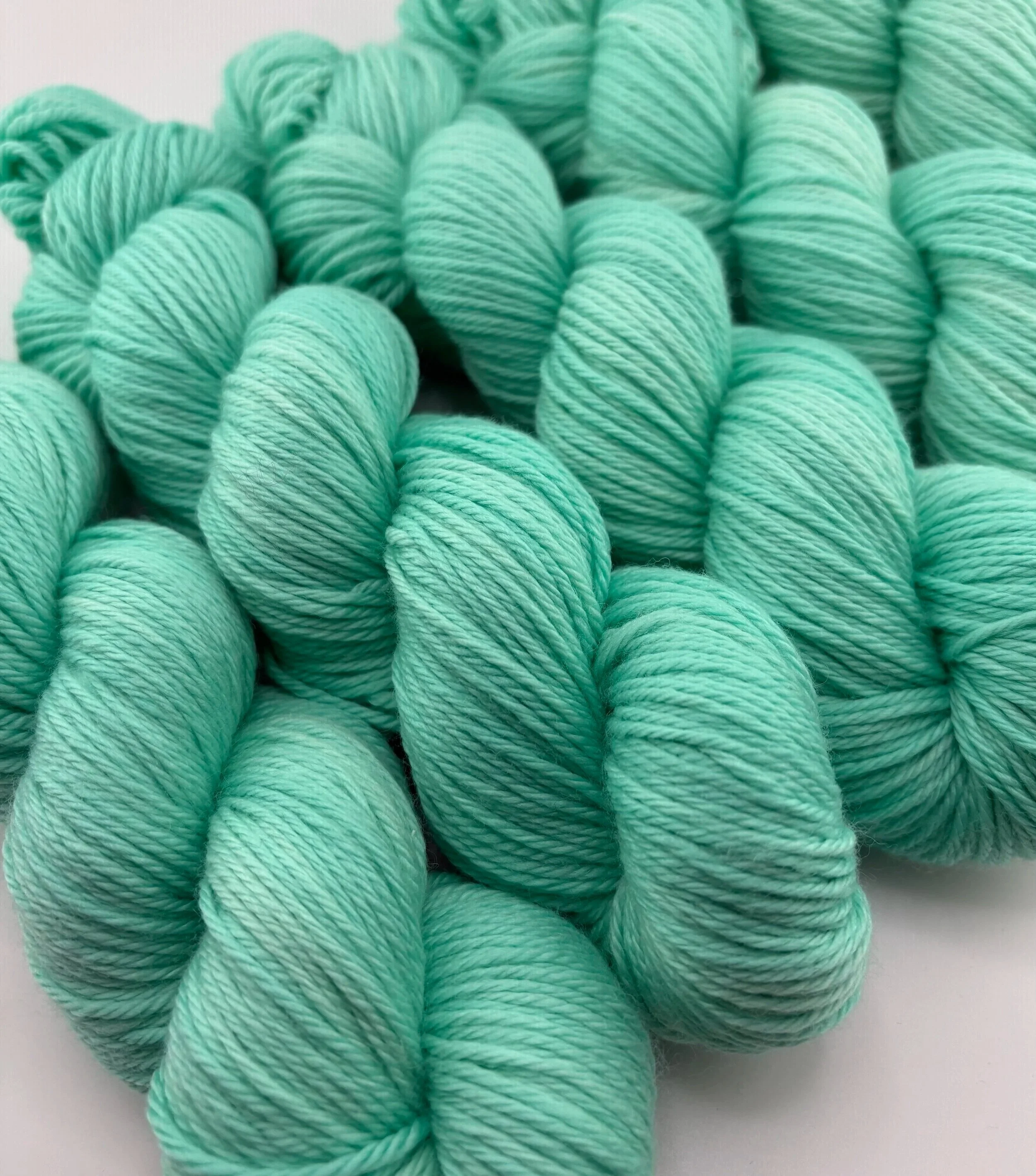A close up of Hand‑dyed yarn skeins in mint green shades arranged in a neat pile.